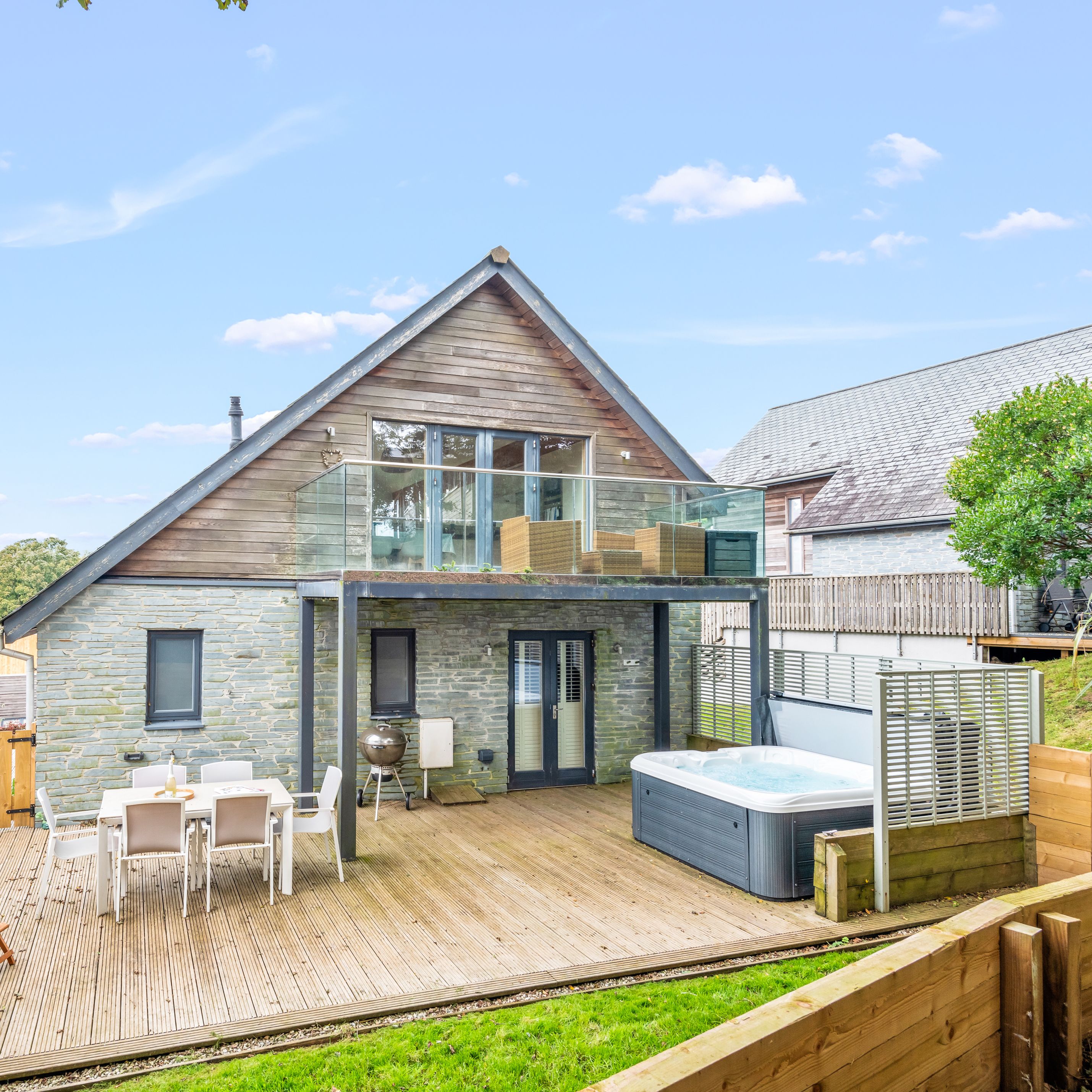 Modern house with stone and wood exterior, large deck, hot tub, outdoor dining area, and upper balcony.