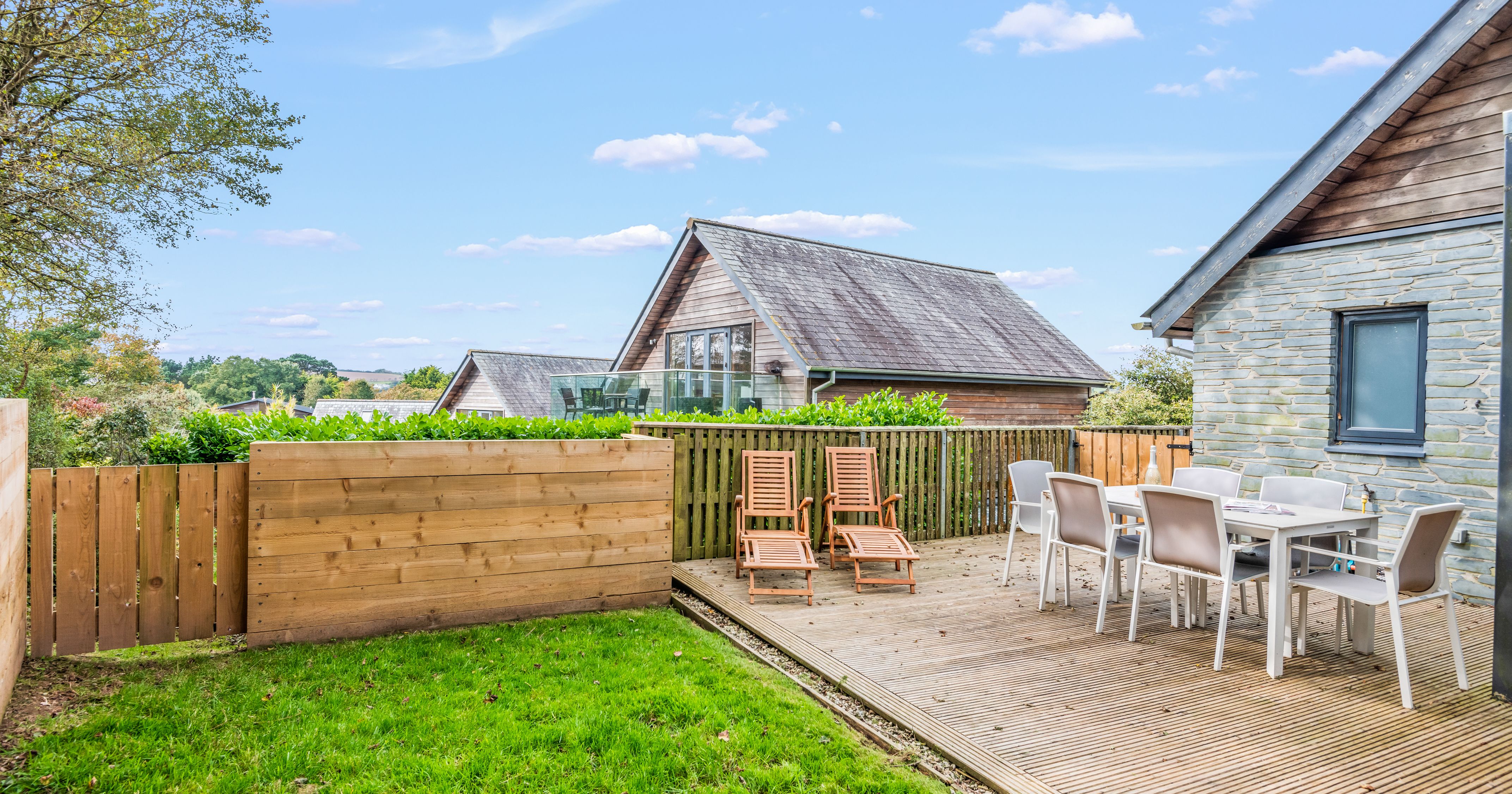 Outdoor patio with wooden deck, two loungers, dining table and chairs, and a fenced garden area