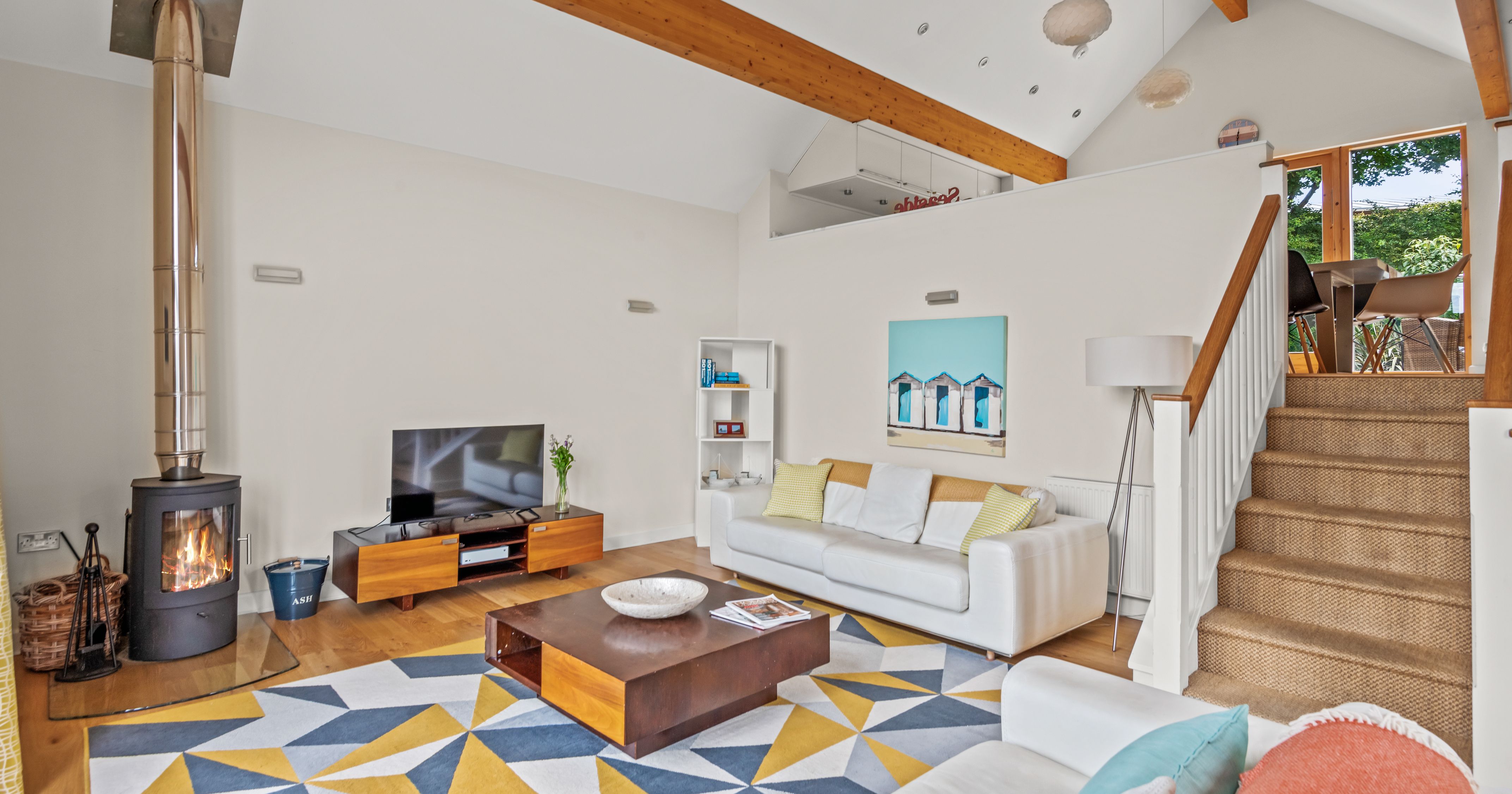 Modern living room with wood stove, geometric rug, white sofas, and split-level dining area.