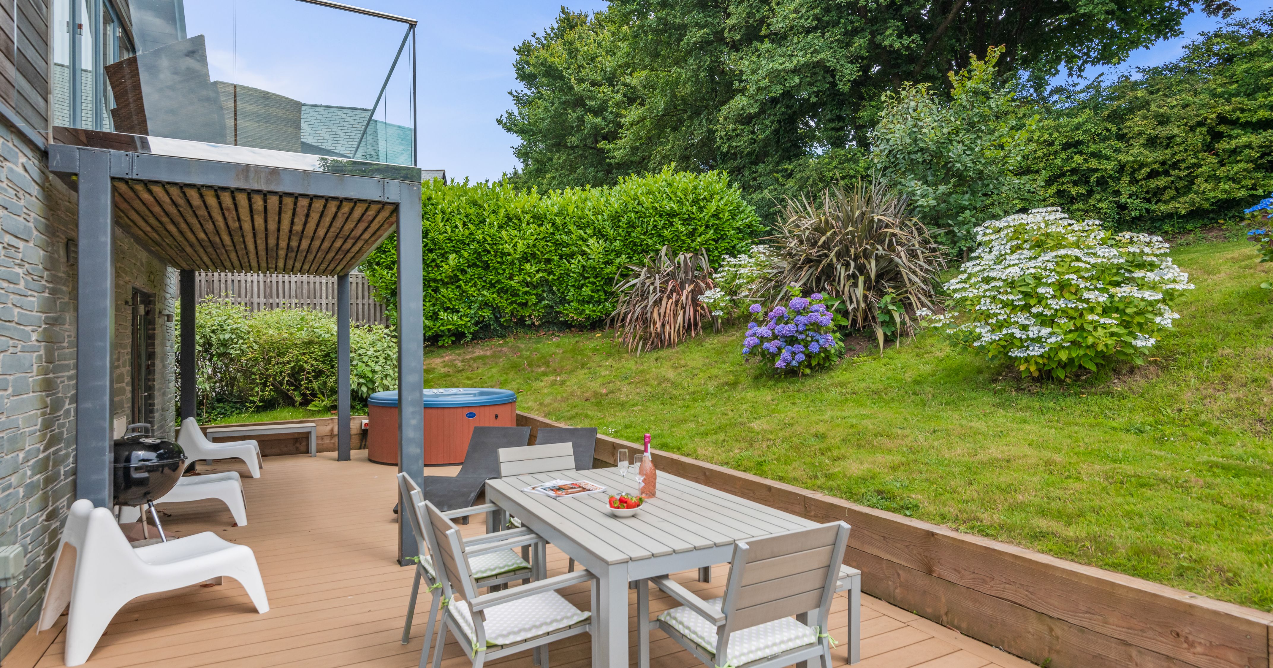 Modern outdoor patio with dining set, hot tub, and lush garden