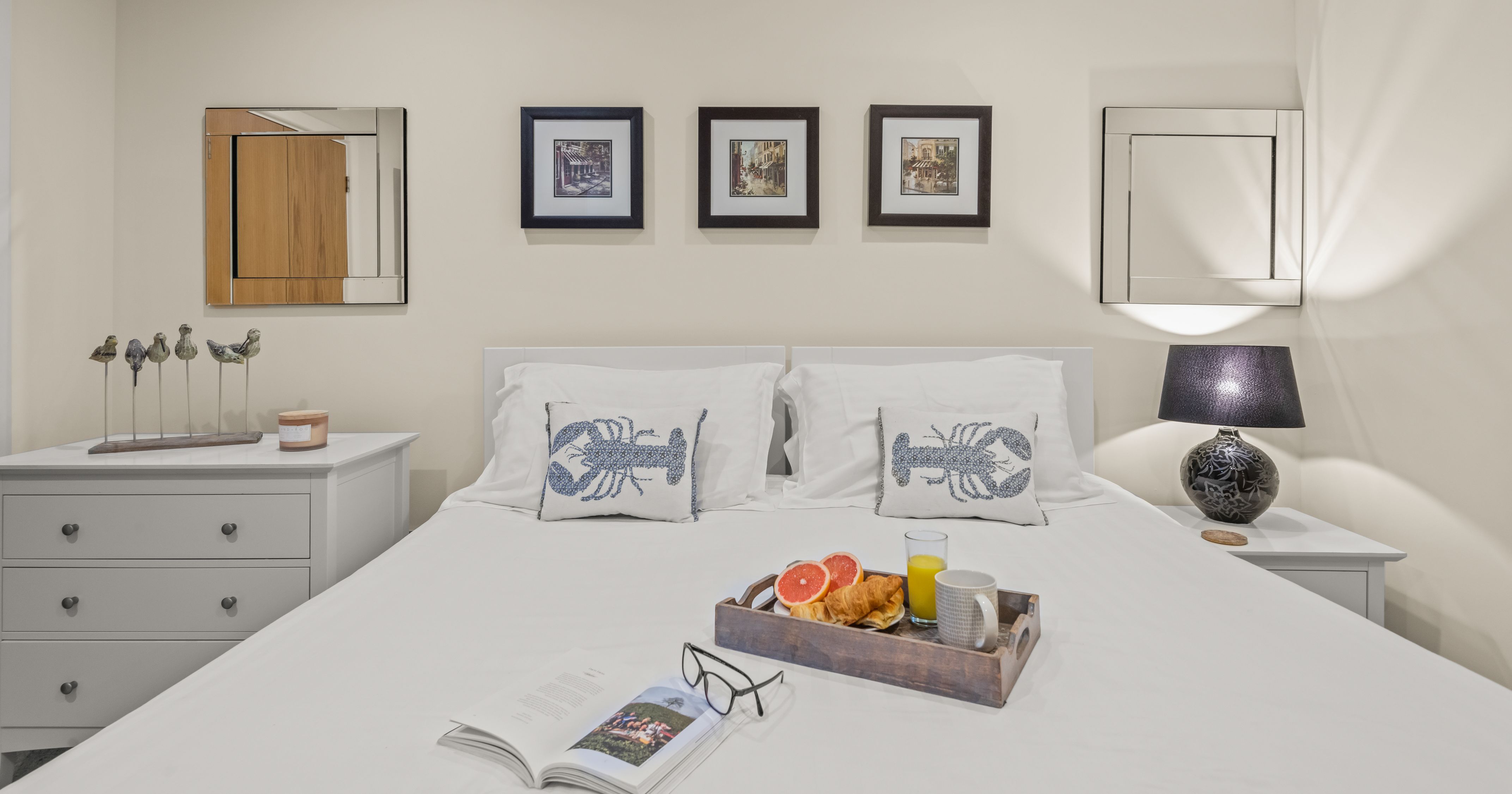 Cozy bedroom with a white bed, lobster pillows, a breakfast tray, and wall art