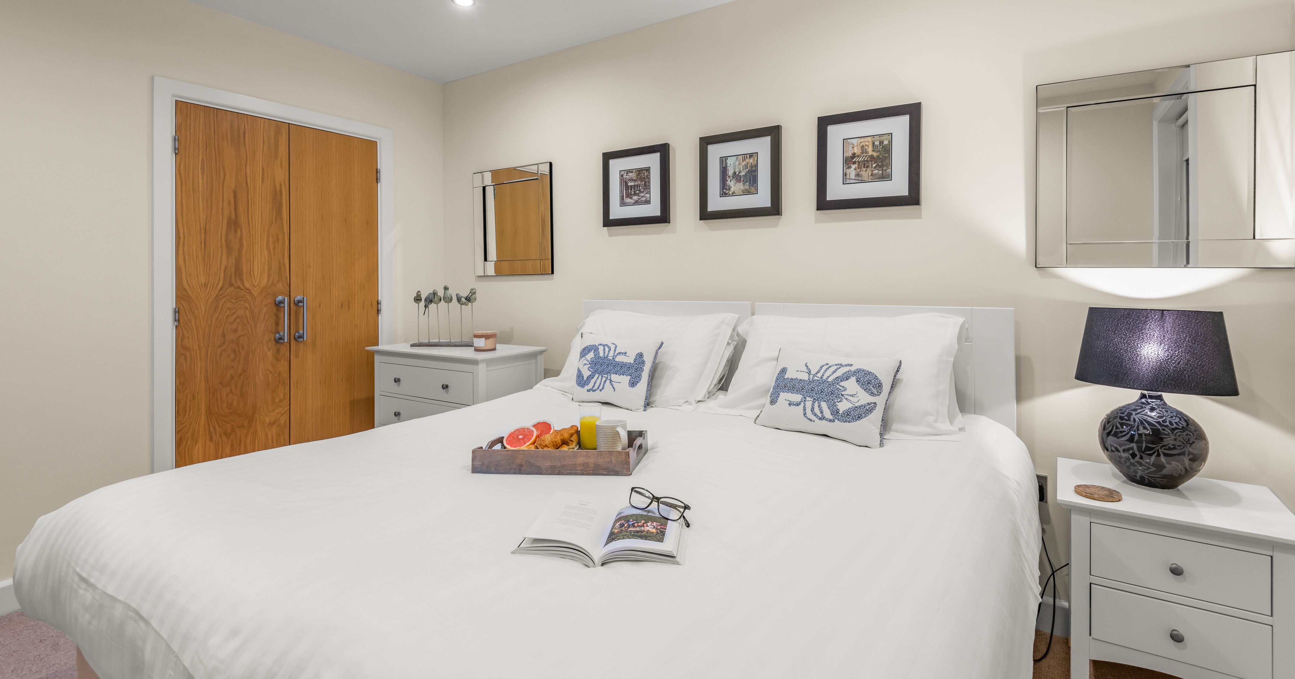 Modern bedroom with white bedding, decorative pillows, and breakfast tray on bed