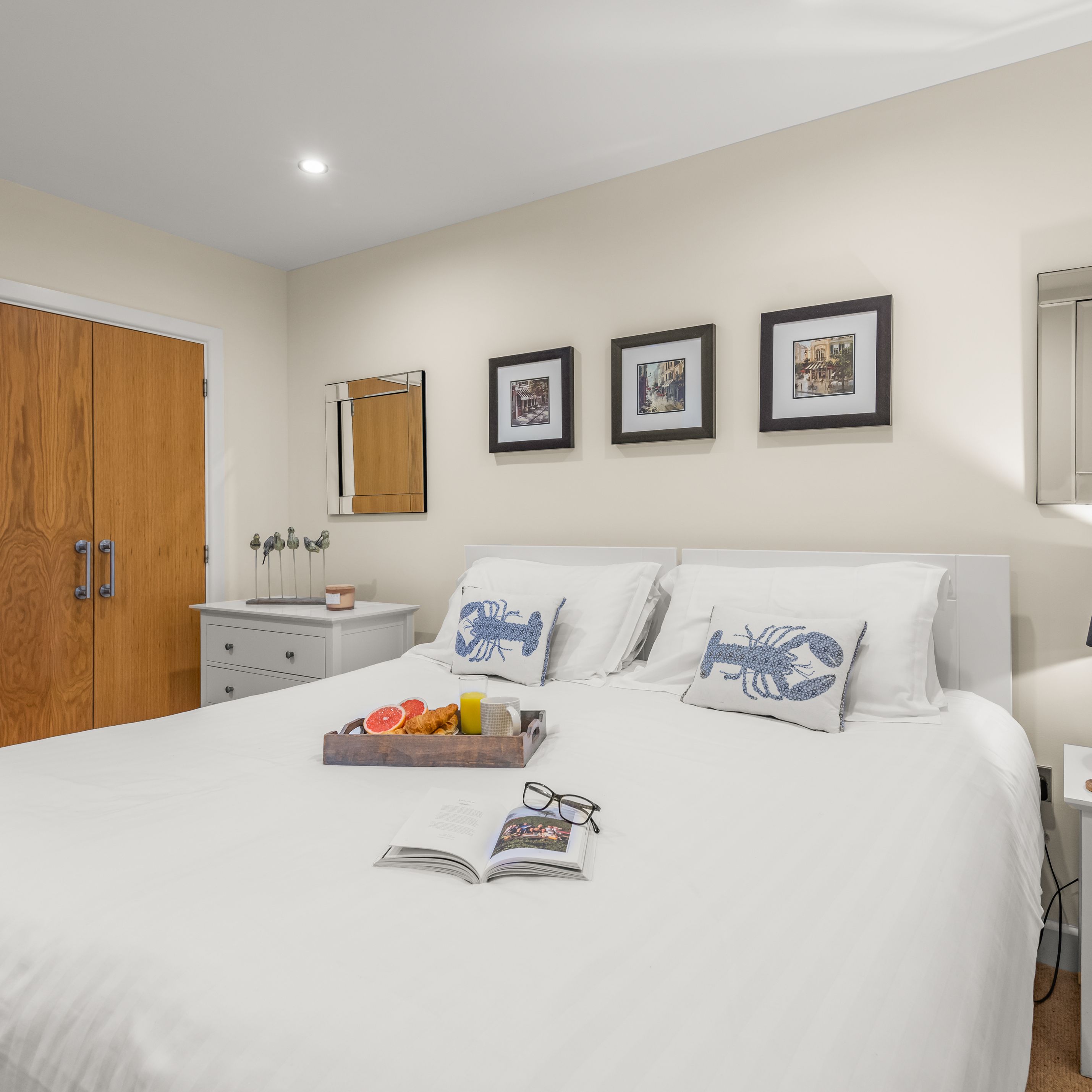 Modern bedroom with white bedding, decorative pillows, and breakfast tray on bed