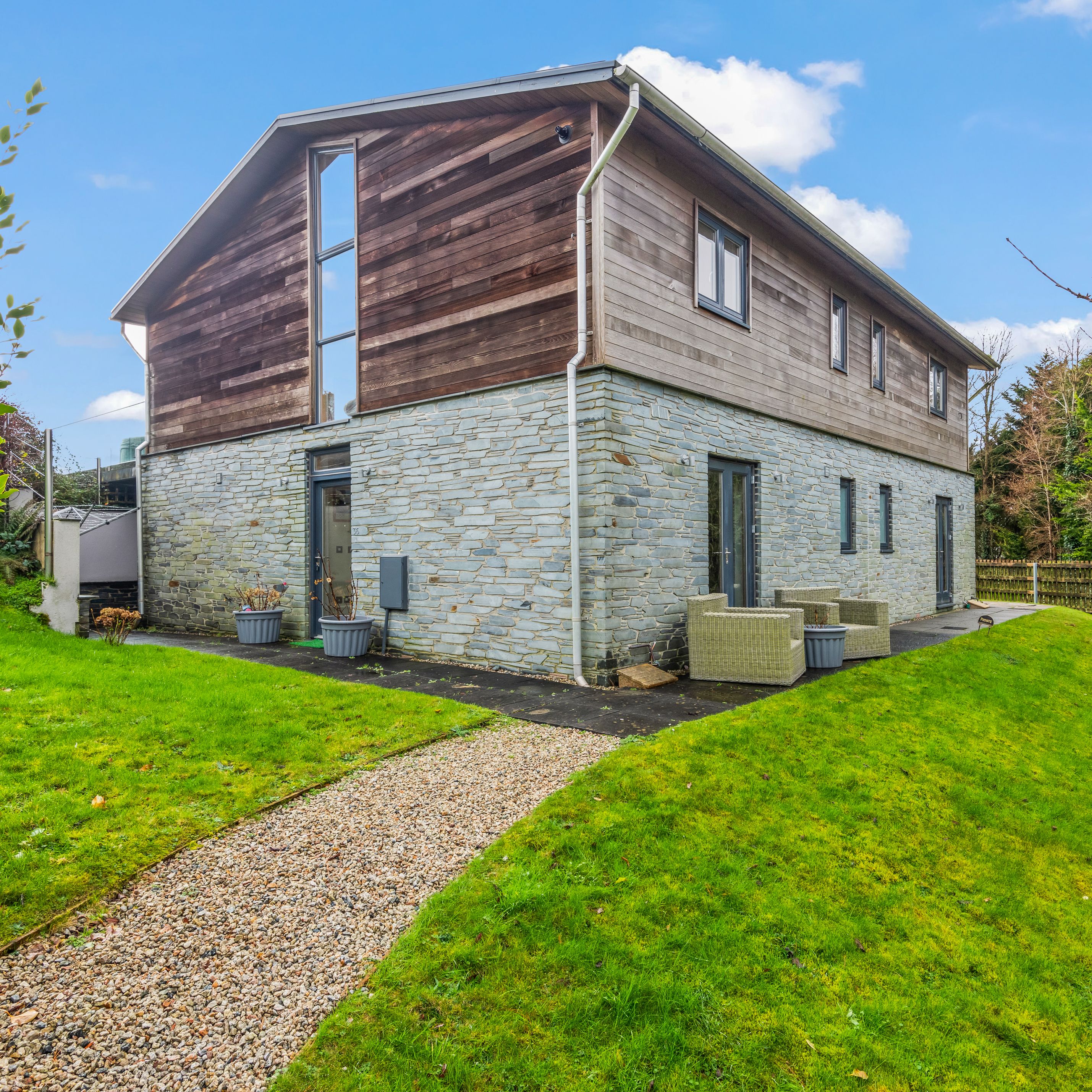 Modern two-story house with stone and wood exterior, surrounded by green lawn and outdoor patio furniture.
