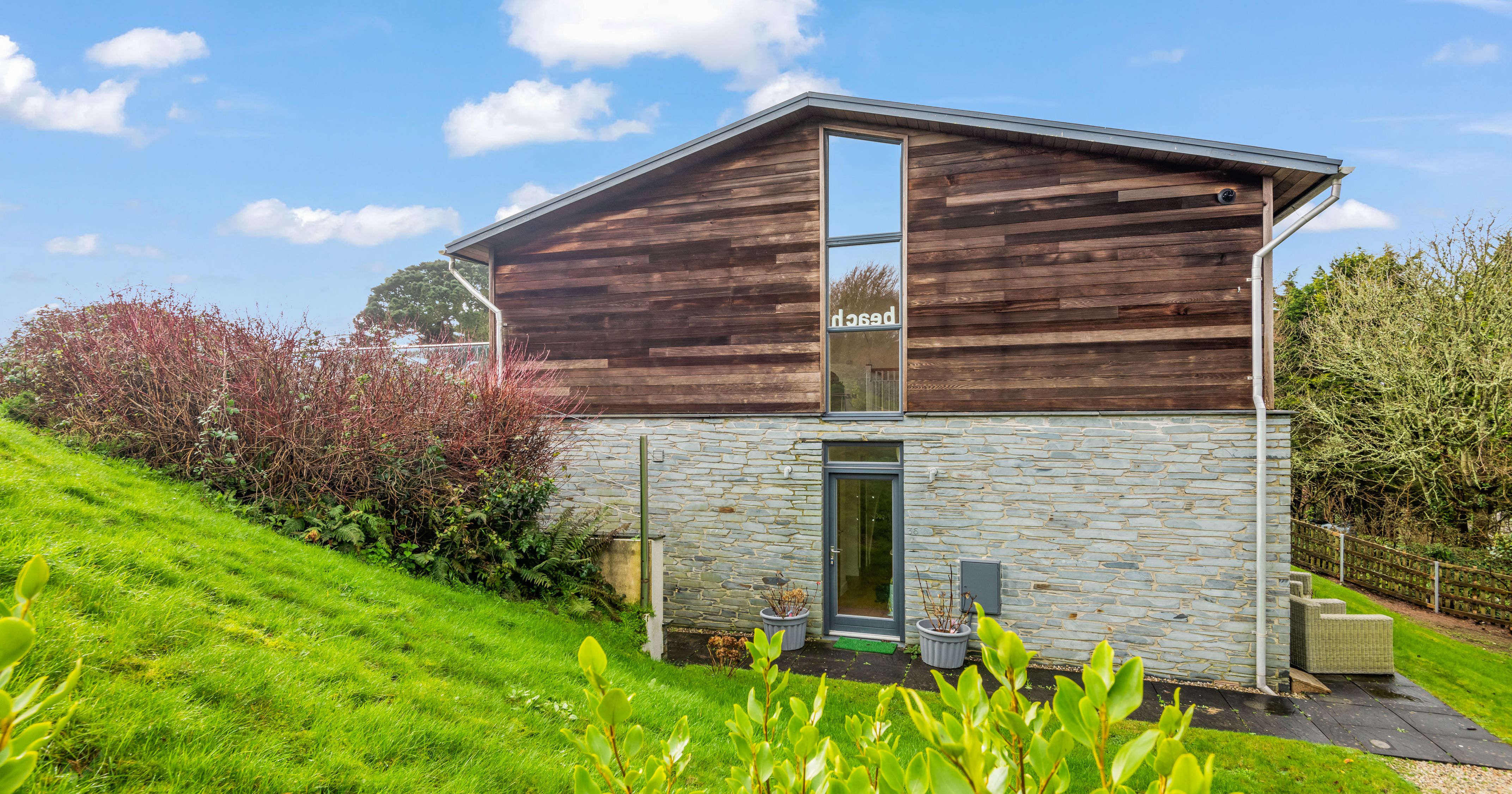 Modern house with wood and stone facade, large window, and green lawn