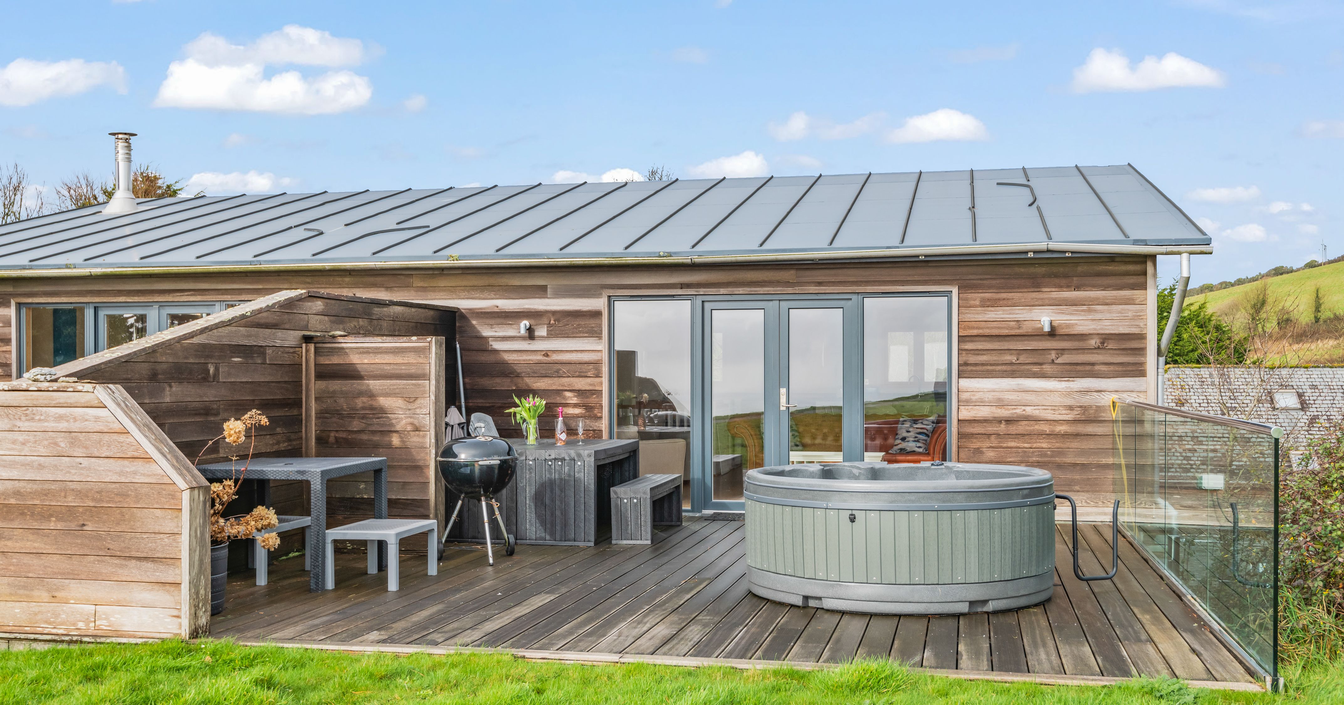 Modern wooden cabin with outdoor deck, grill, and hot tub