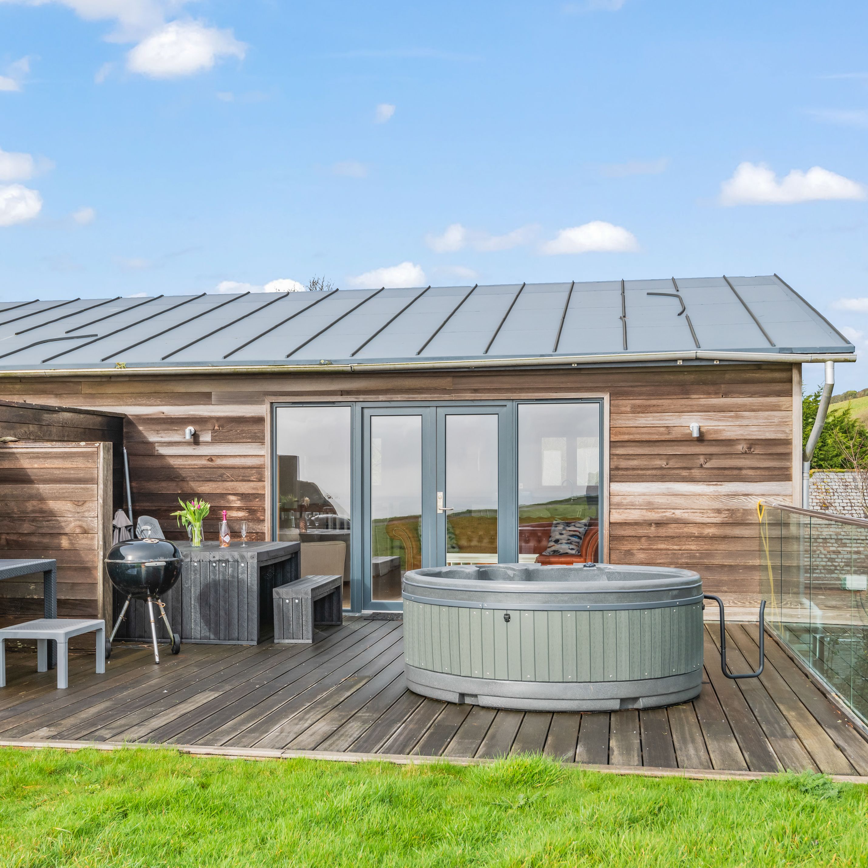 Modern wooden cabin with outdoor deck, grill, and hot tub