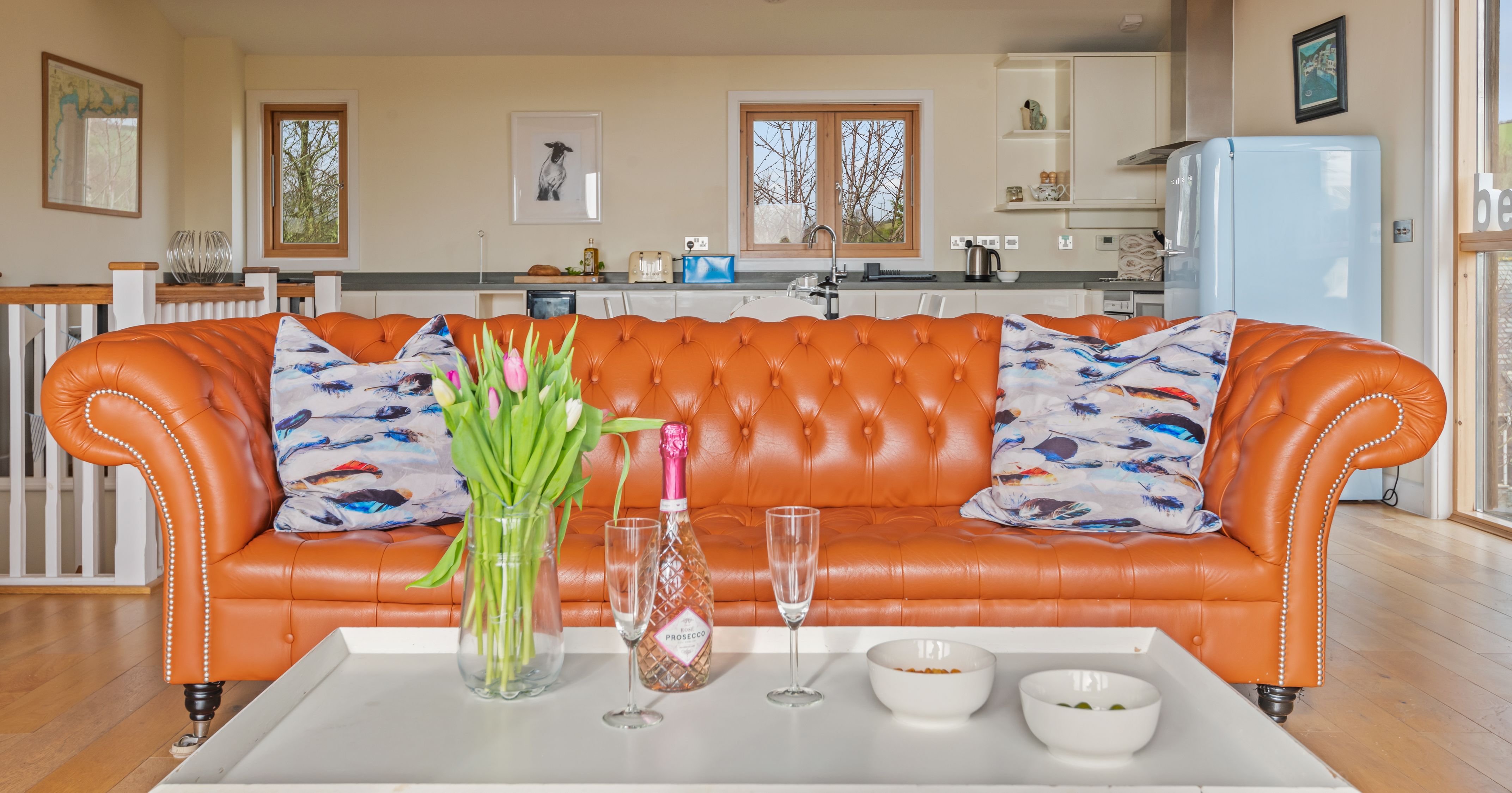 Bright orange leather sofa in a modern open-plan living room with a kitchen in the background.