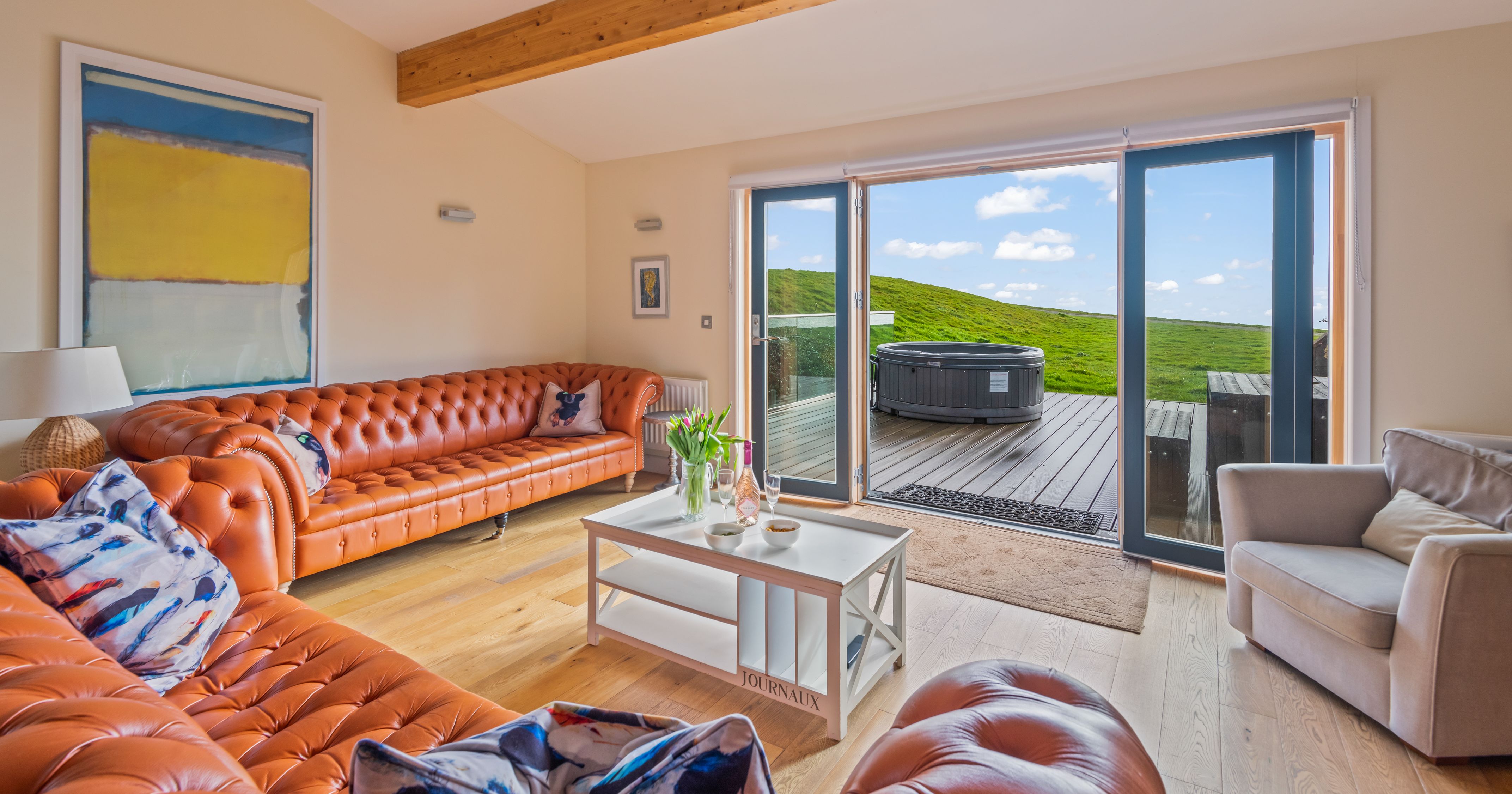 Modern living room with orange leather sofas, large windows, and outdoor hot tub