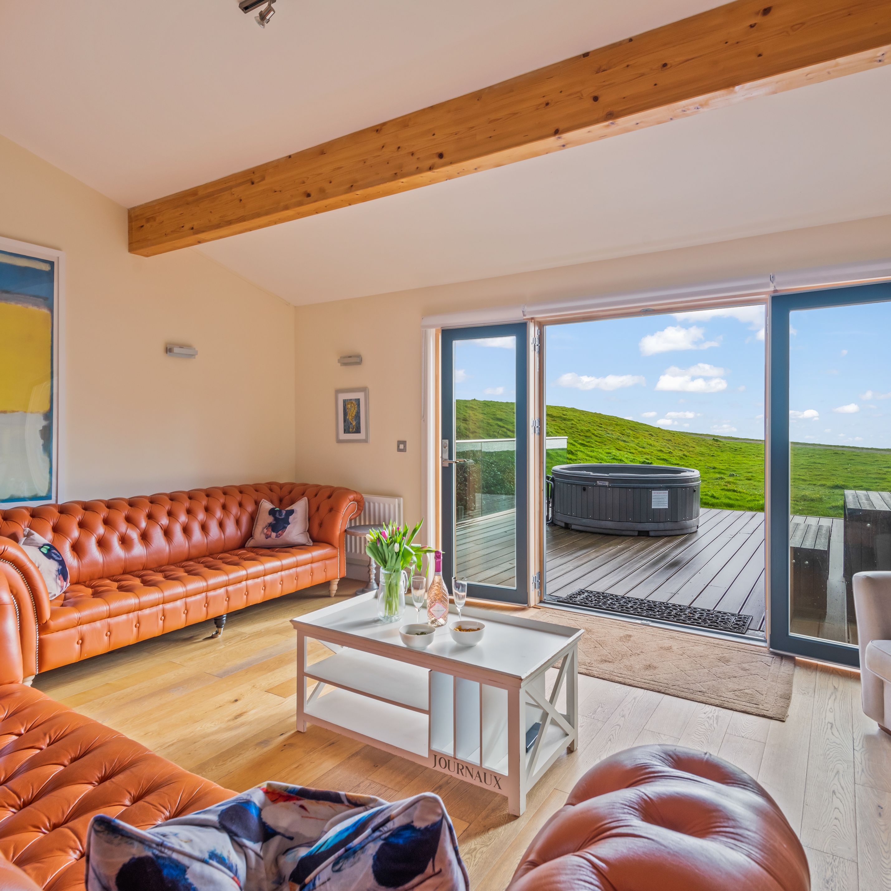 Modern living room with orange leather sofas, large windows, and outdoor hot tub