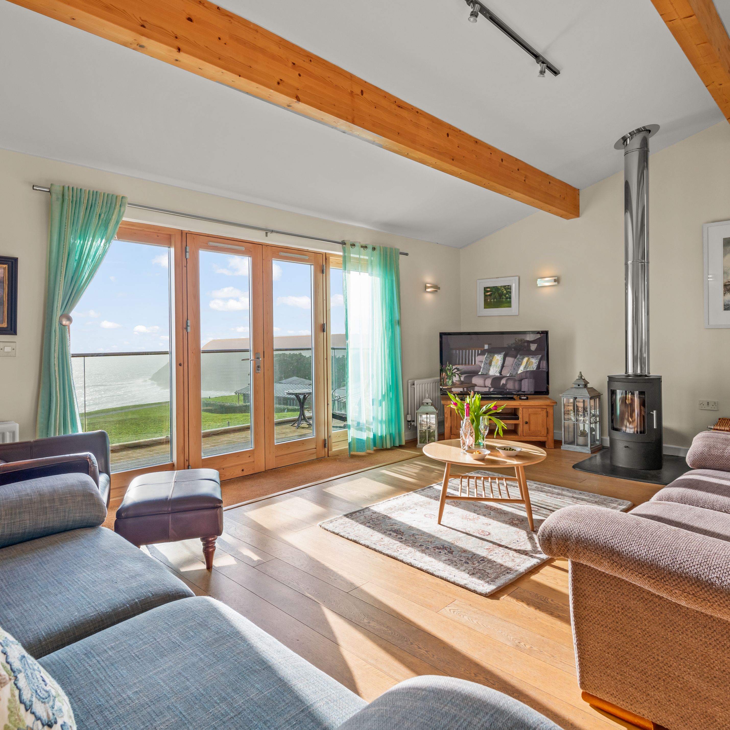 Bright living room with large glass doors overlooking the ocean, cozy seating, a wood-burning stove, and a television.