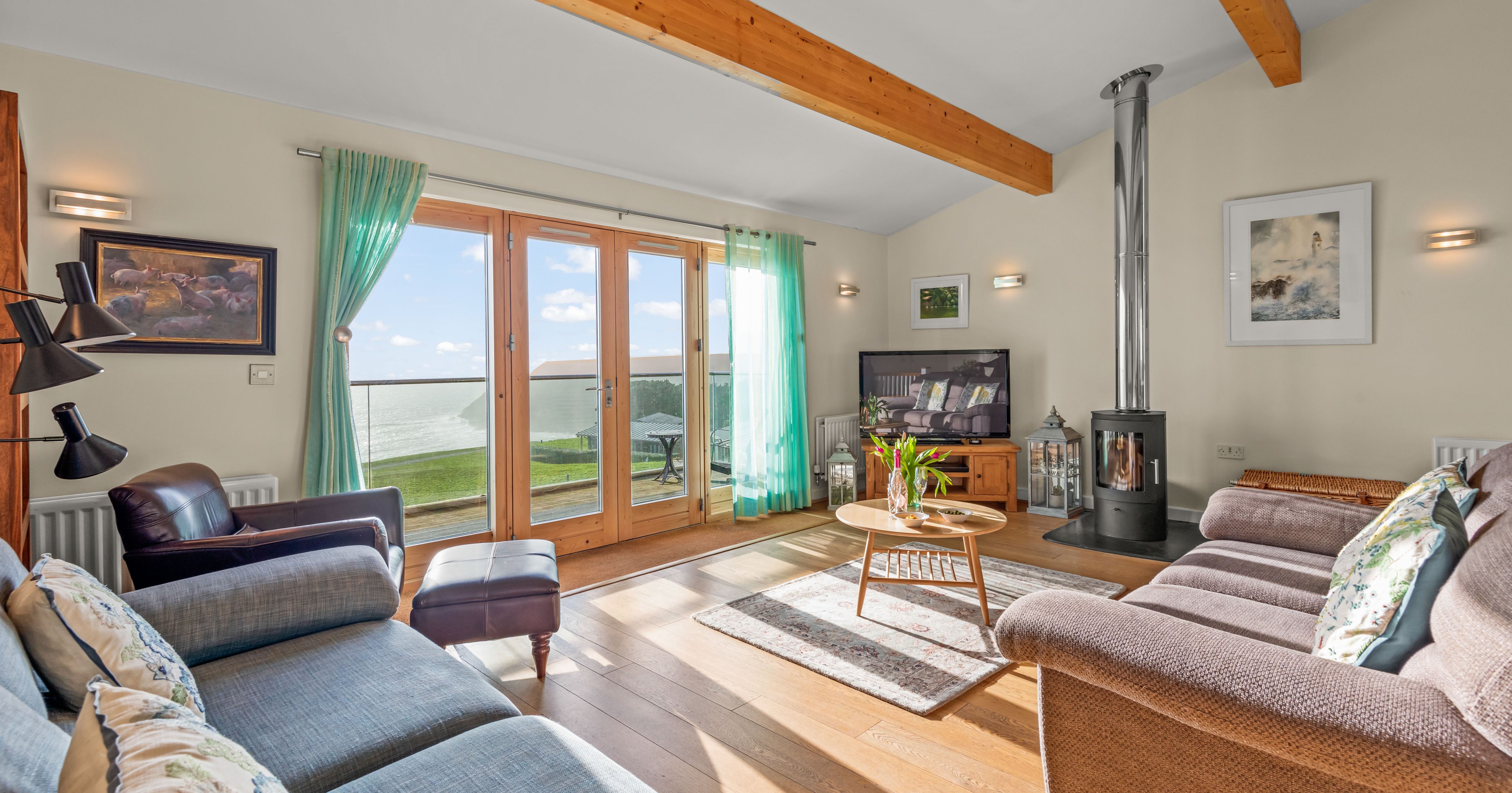 Bright living room with large glass doors overlooking the ocean, cozy seating, a wood-burning stove, and a television.