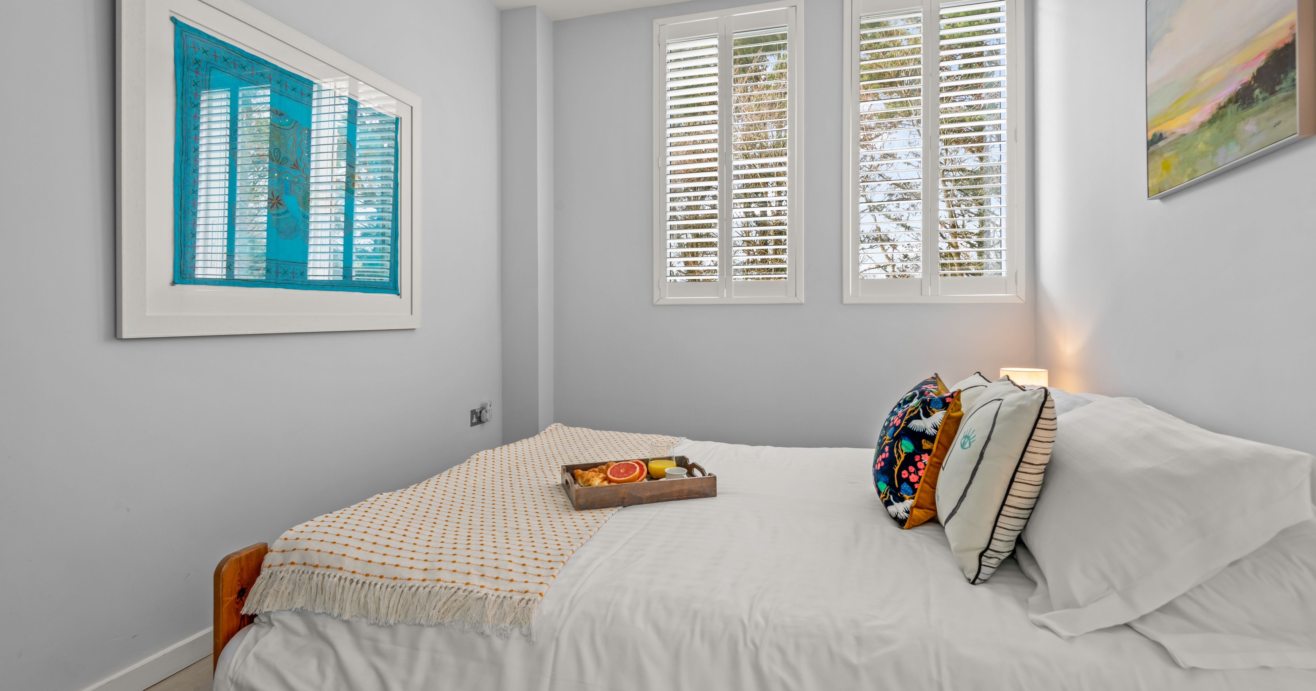 Cozy bedroom with white bedding, colorful pillows, and breakfast tray
