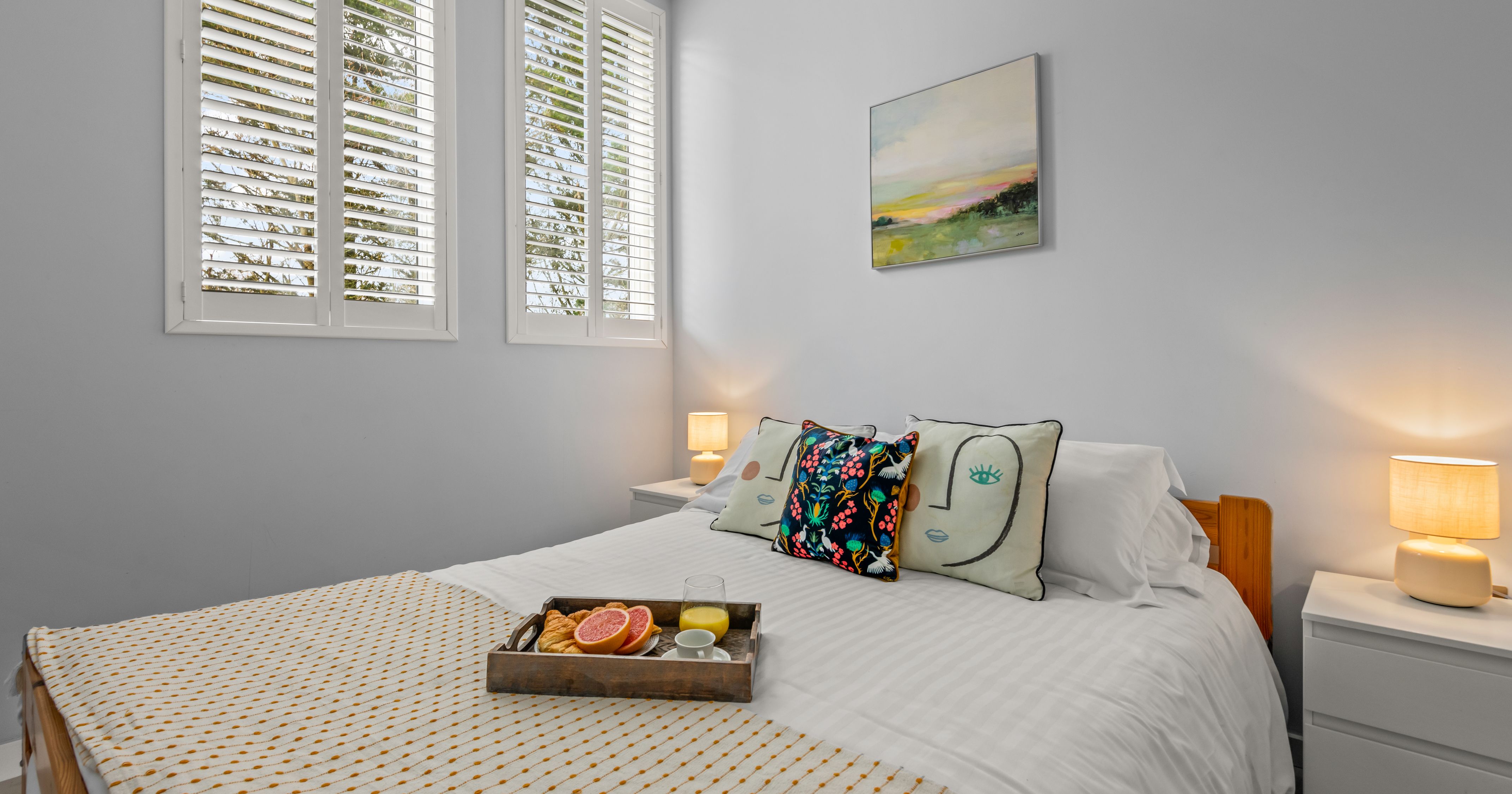 Cozy bedroom with a neatly made bed, decorative pillows, bedside tables with lamps, and breakfast tray