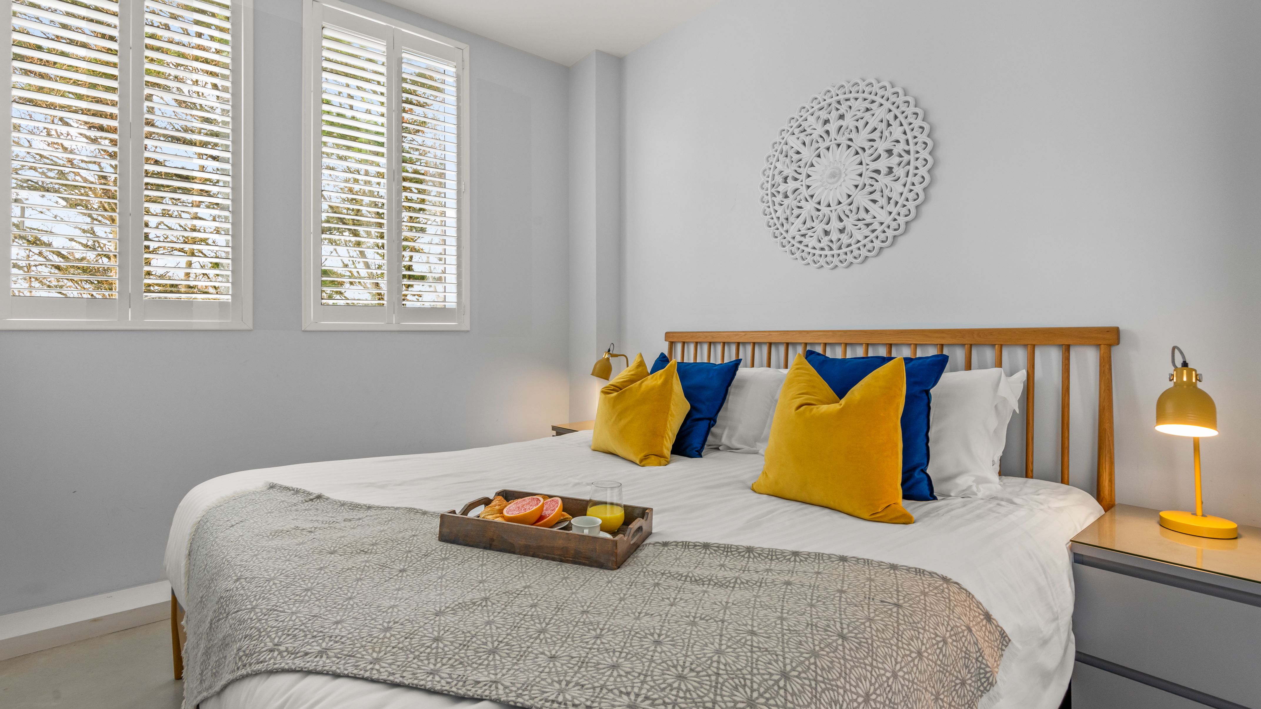 Modern bedroom with yellow and blue pillows and a breakfast tray on the bed