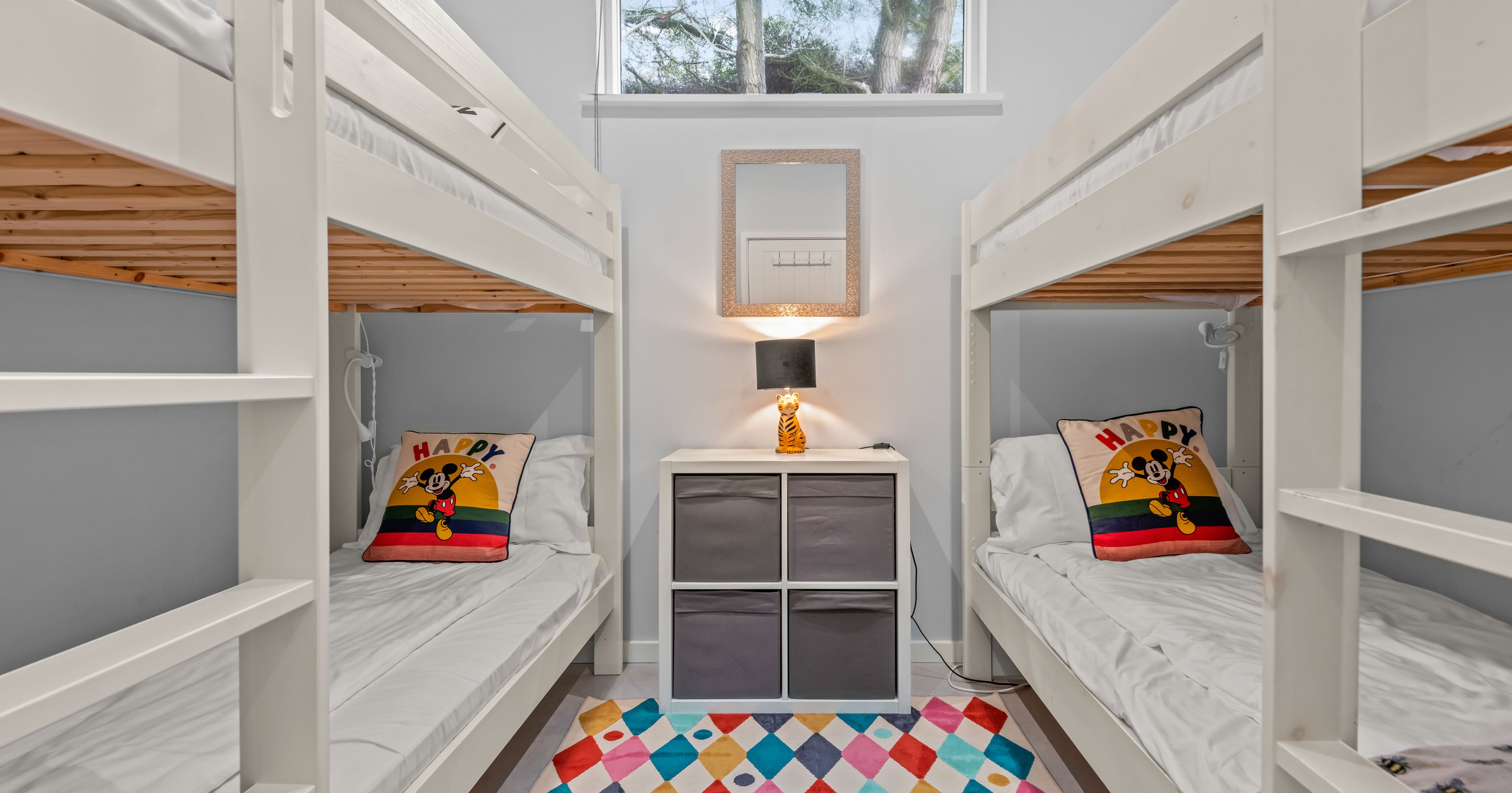 Children's bedroom with two white bunk beds, colorful rug, and Mickey Mouse pillows