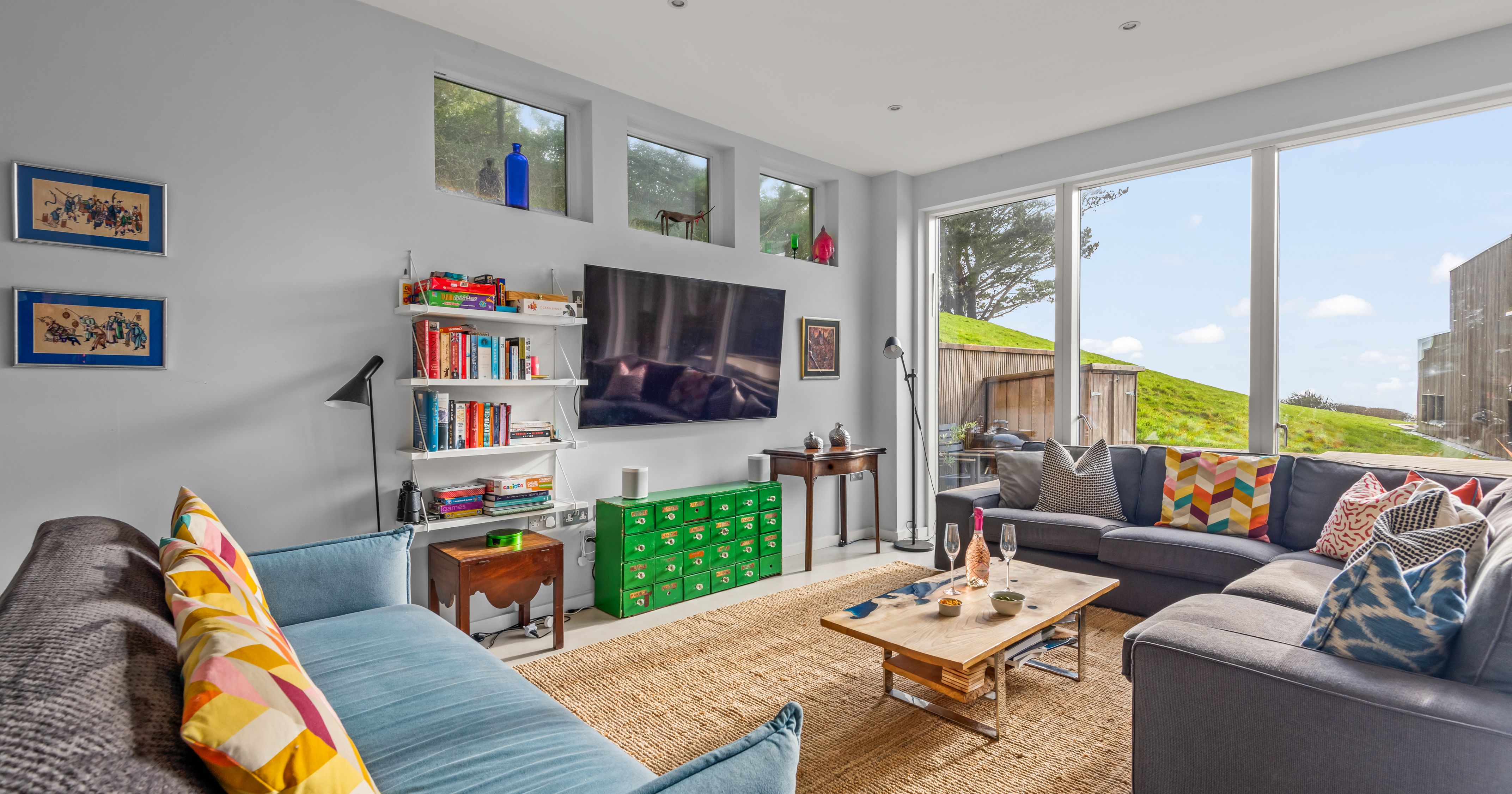 Modern living room with colorful pillows, large windows, and a television on the wall