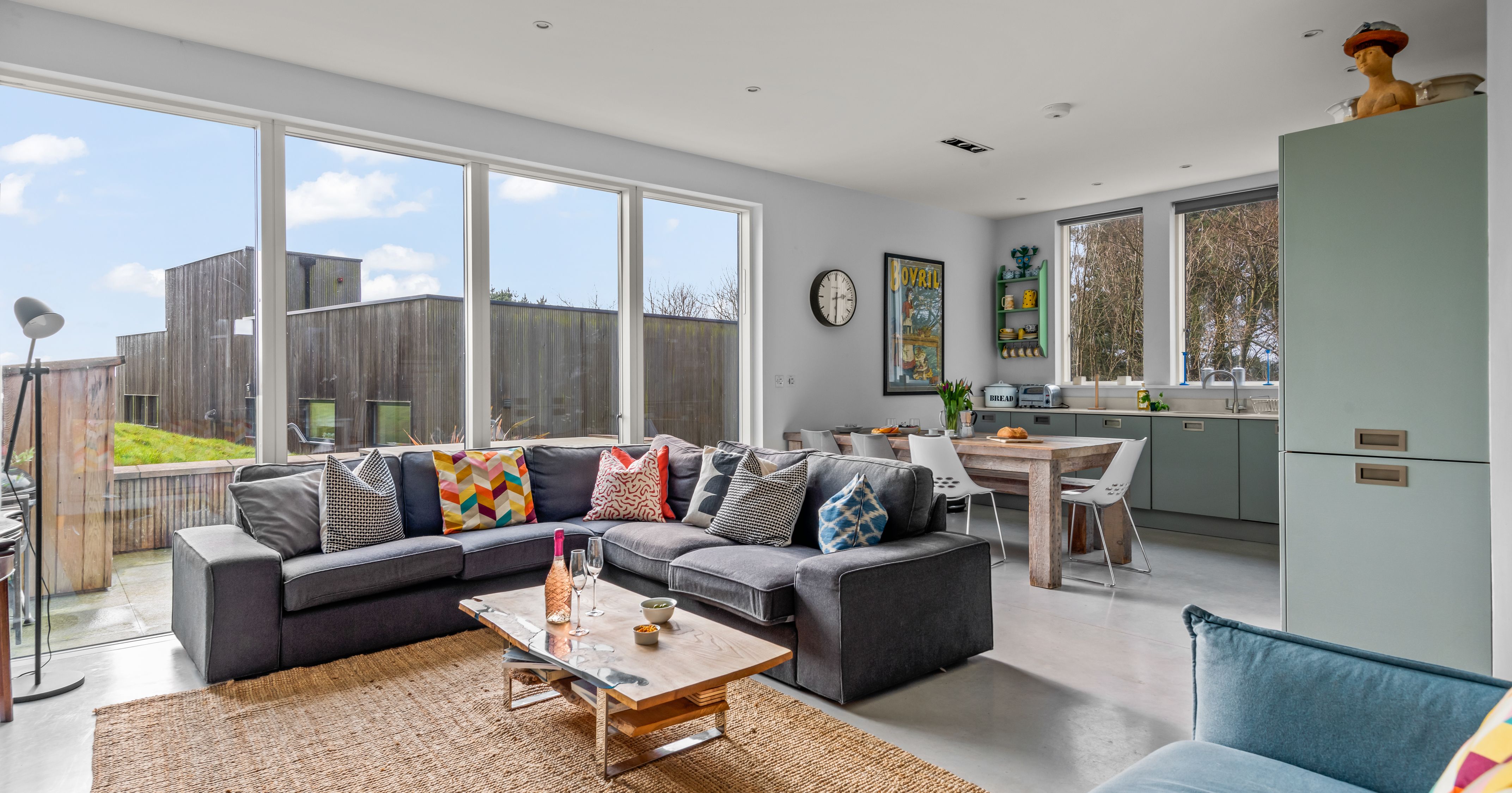 Modern open-plan living room and kitchen with large windows and colorful furniture