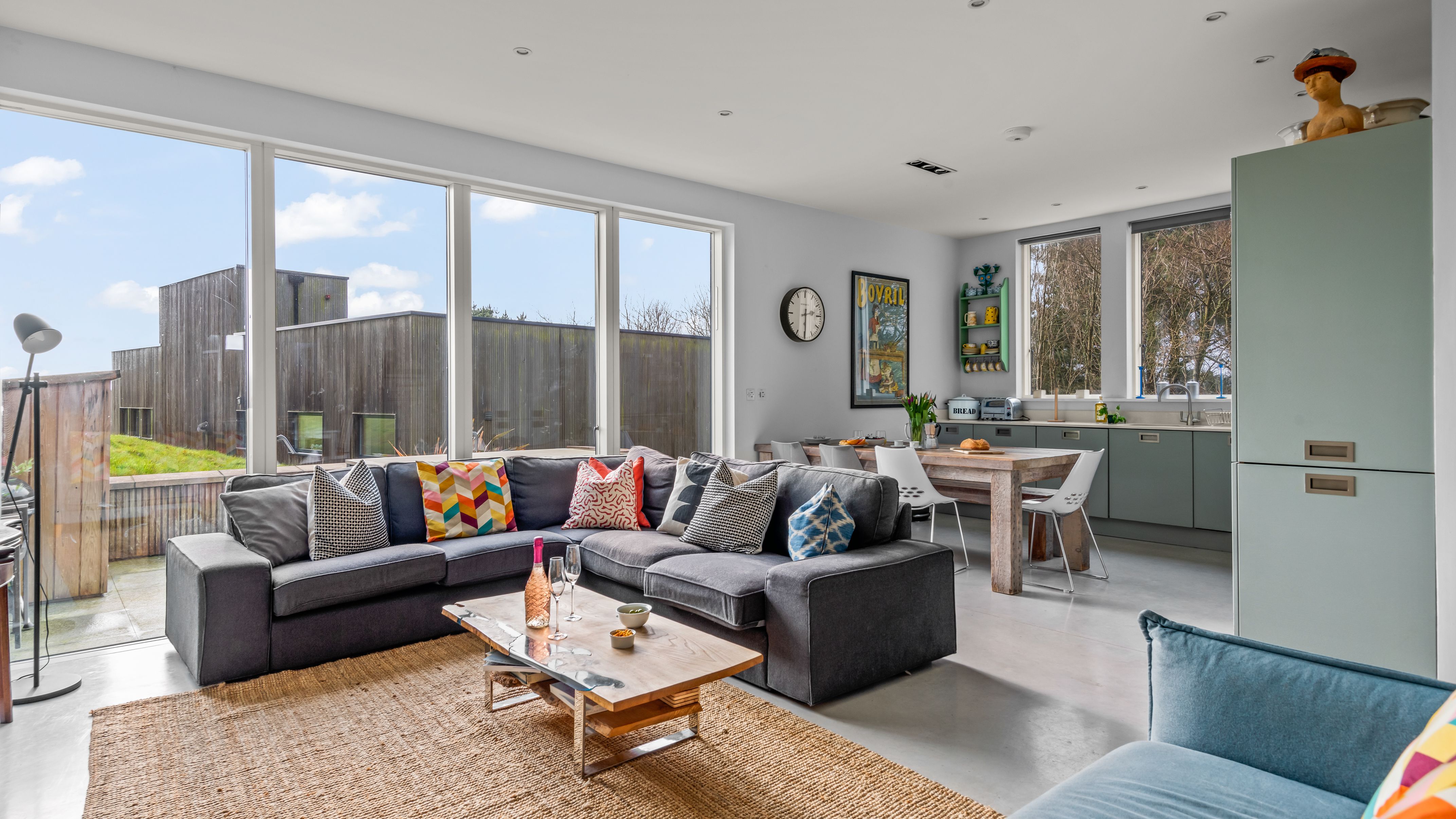 Modern open-plan living room and kitchen with large windows and colorful furniture