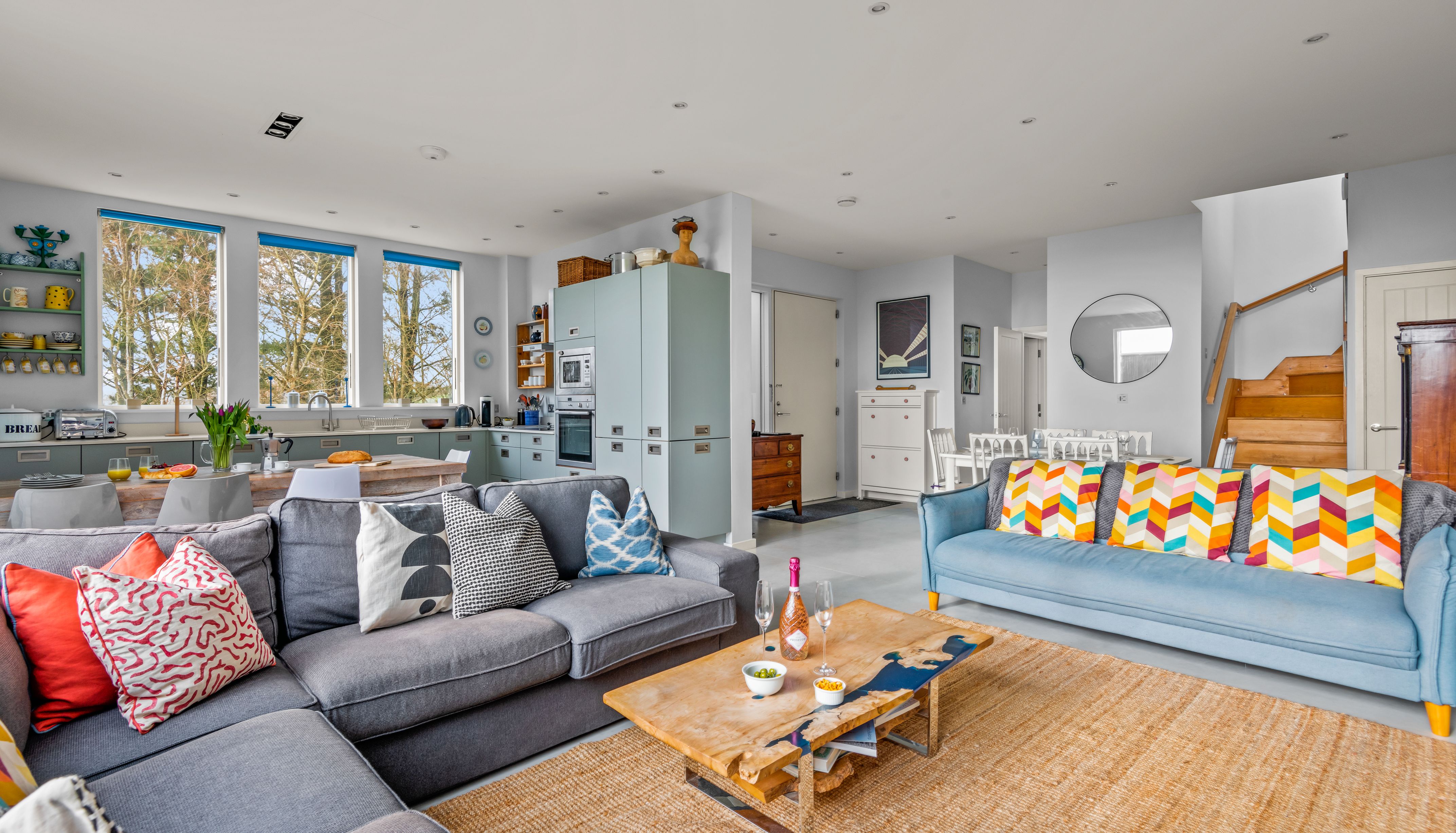 Modern open-plan living room and kitchen with colorful pillows and wooden furniture.