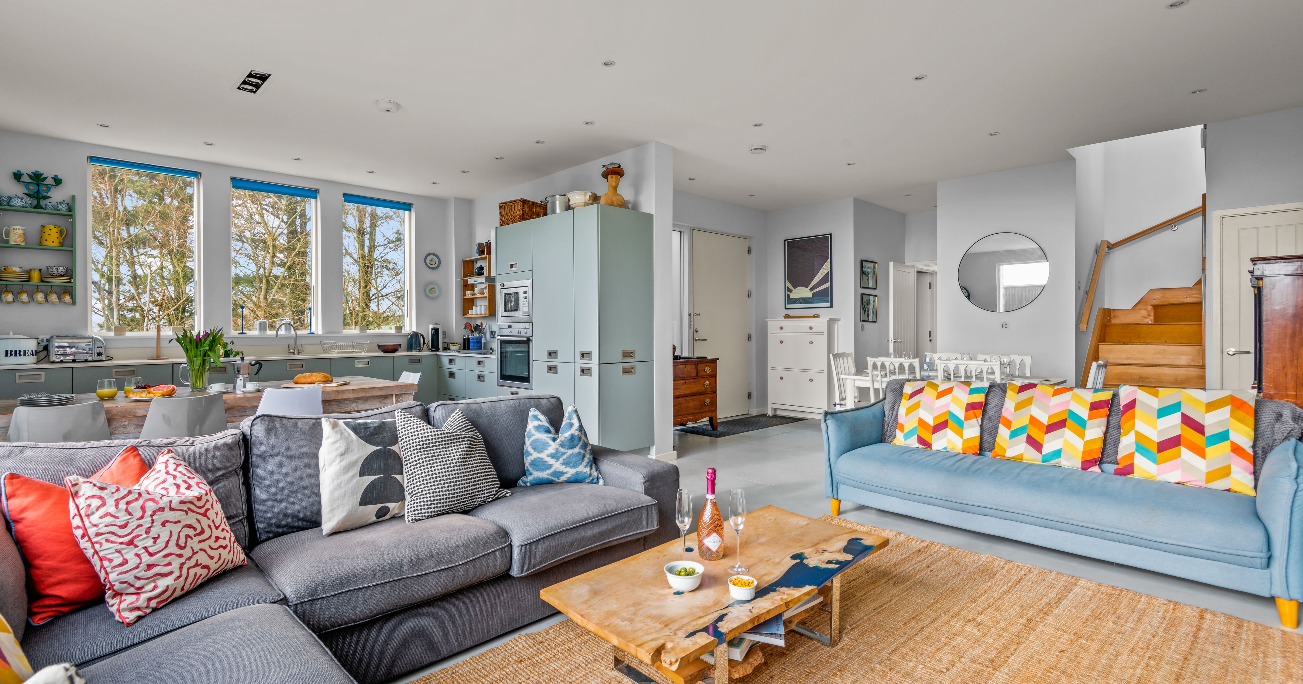 Modern open-plan living room and kitchen with colorful pillows and wooden furniture.