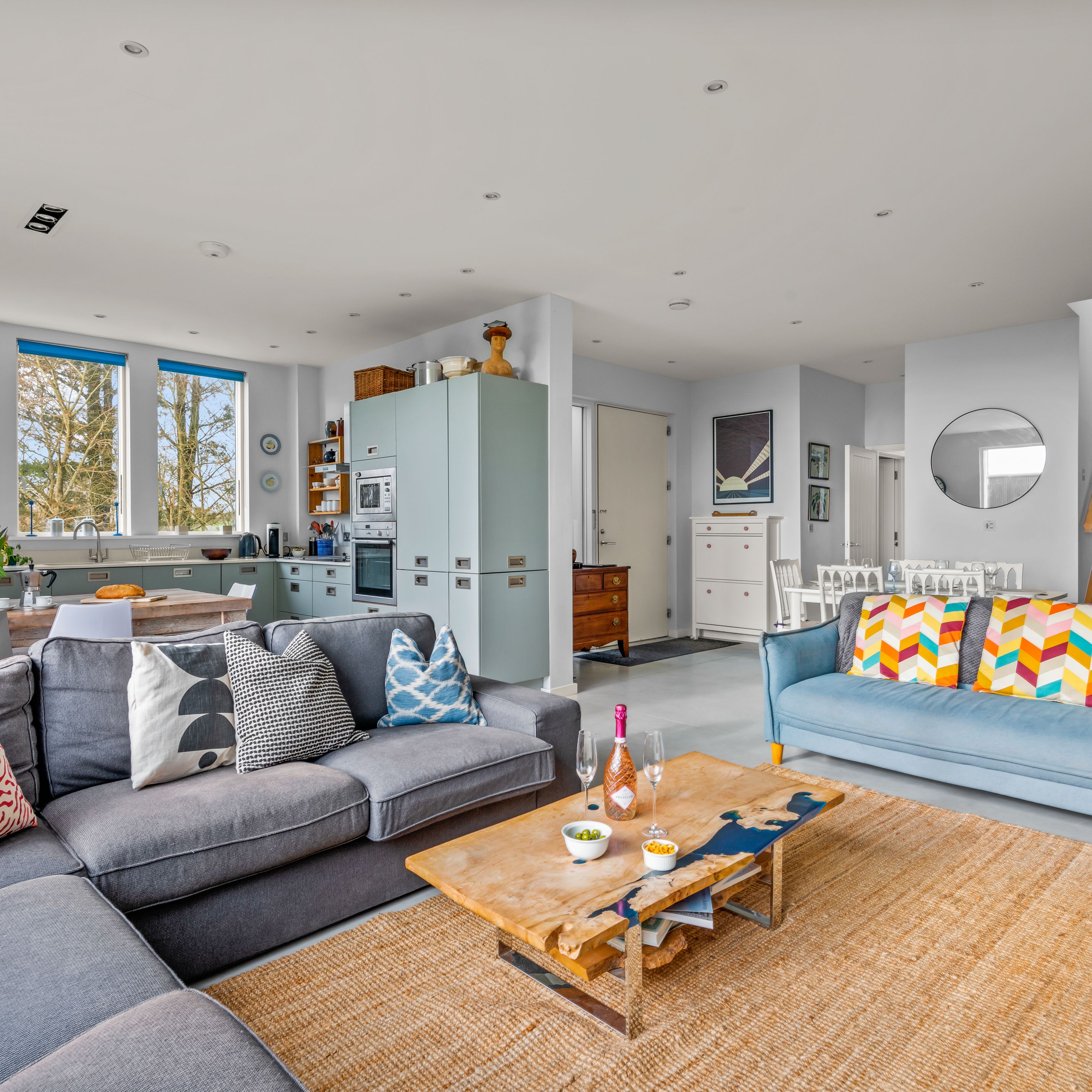 Modern open-plan living room and kitchen with colorful pillows and wooden furniture.
