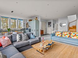 Modern open-plan living room and kitchen with colorful pillows and wooden furniture.