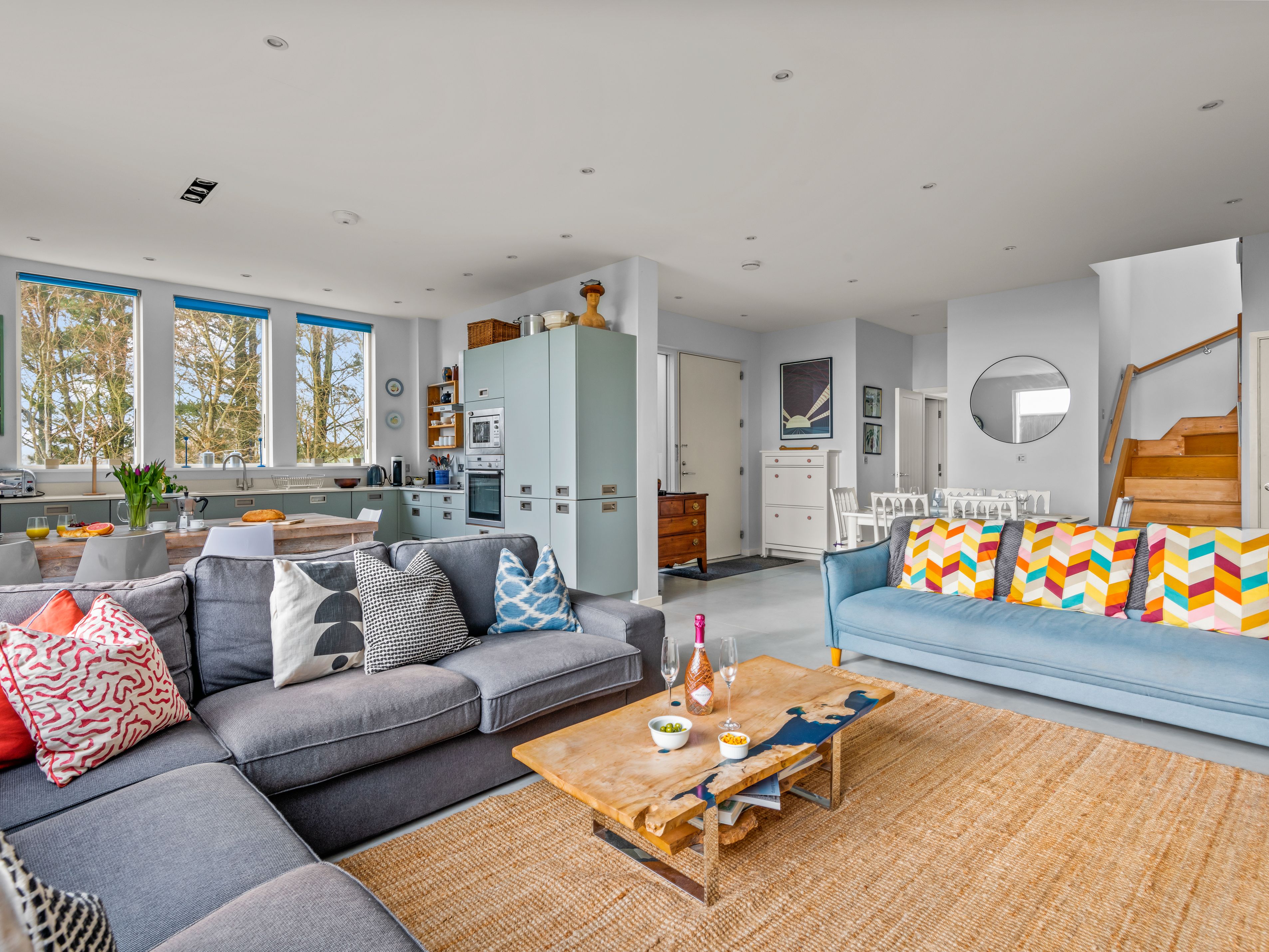 Modern open-plan living room and kitchen with colorful pillows and wooden furniture.