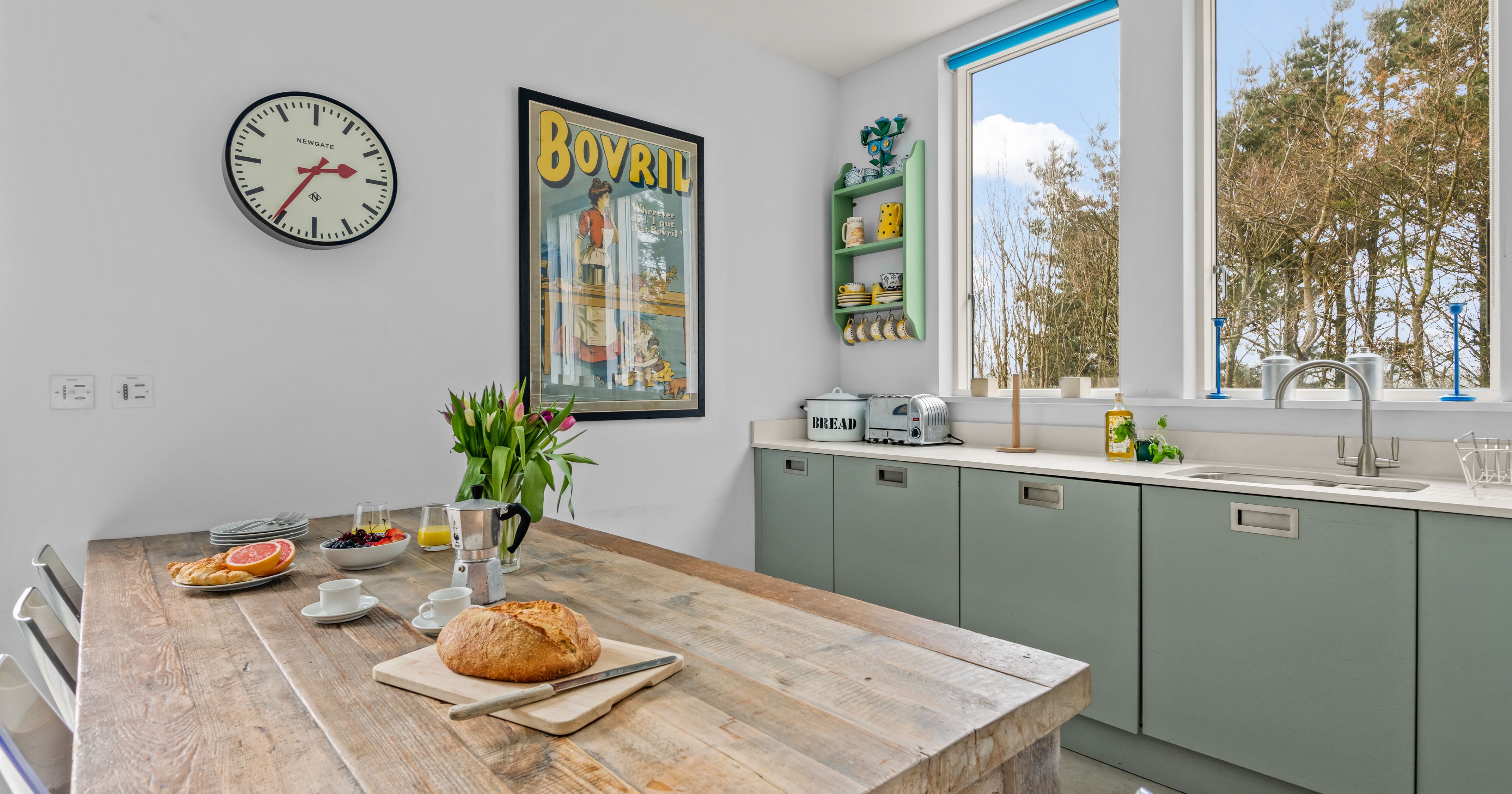 Bright kitchen with rustic wooden table, bread loaf, and large windows overlooking trees