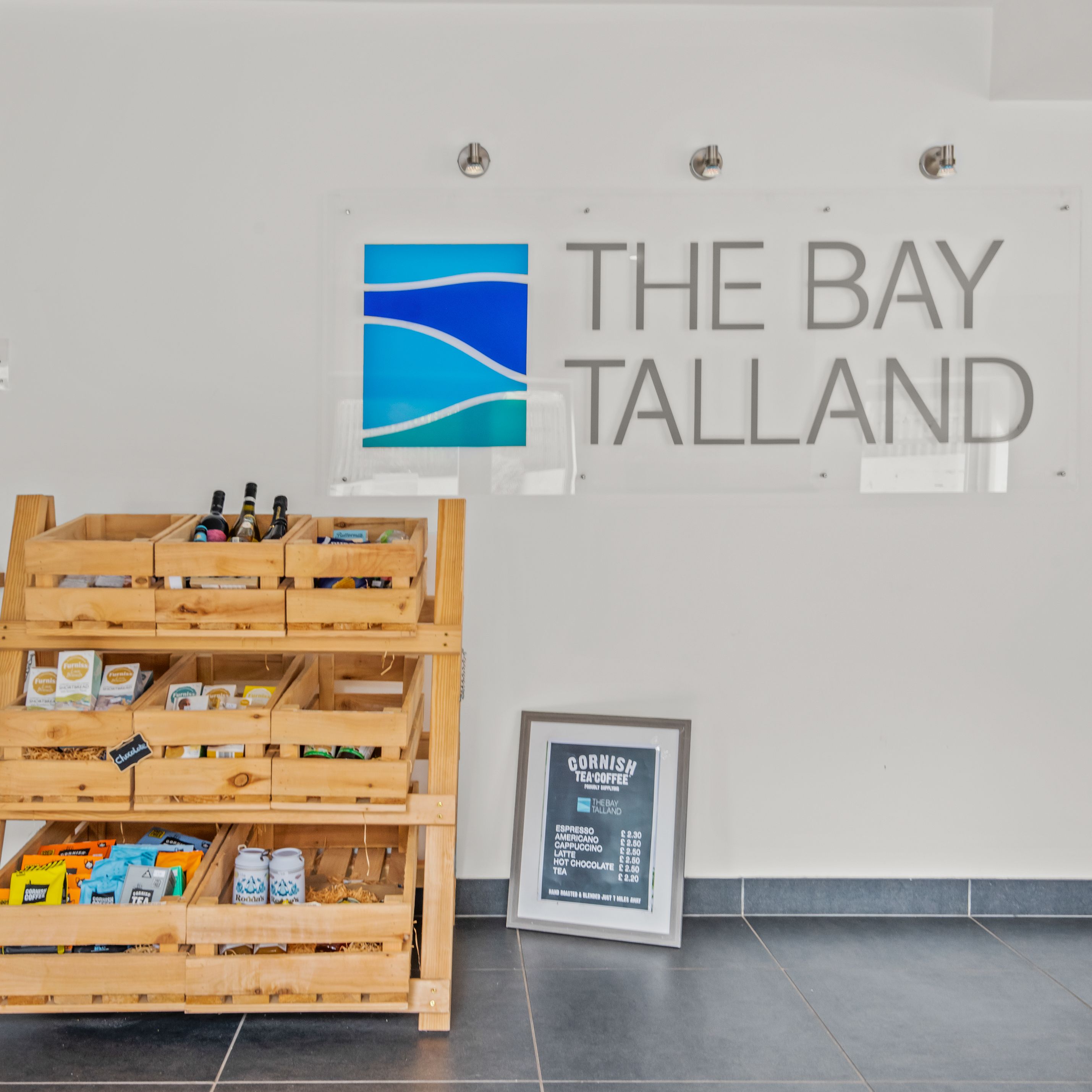 The Bay Talland sign on a wall above wooden shelves with products and a framed menu