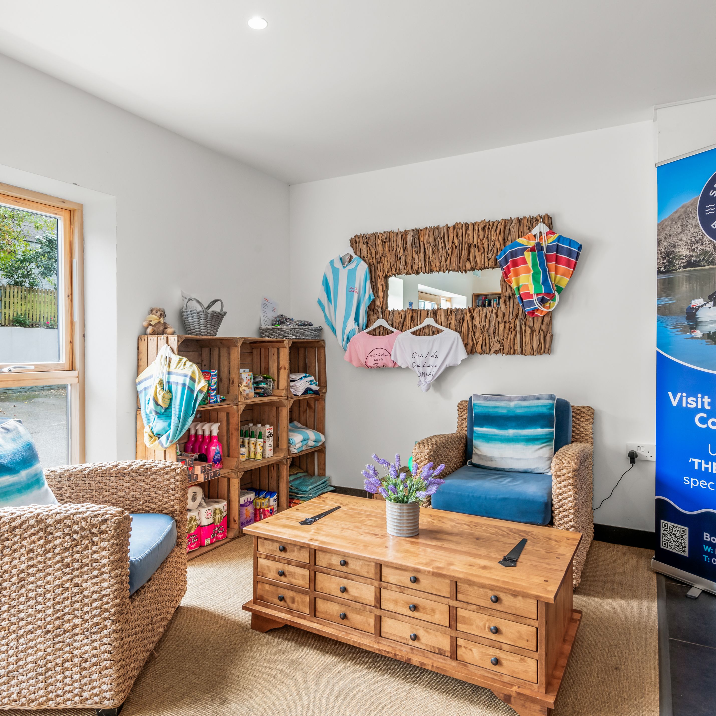 Cozy waiting area with wicker chairs, a wooden coffee table, a promotional banner, and shelves displaying clothing and items.
