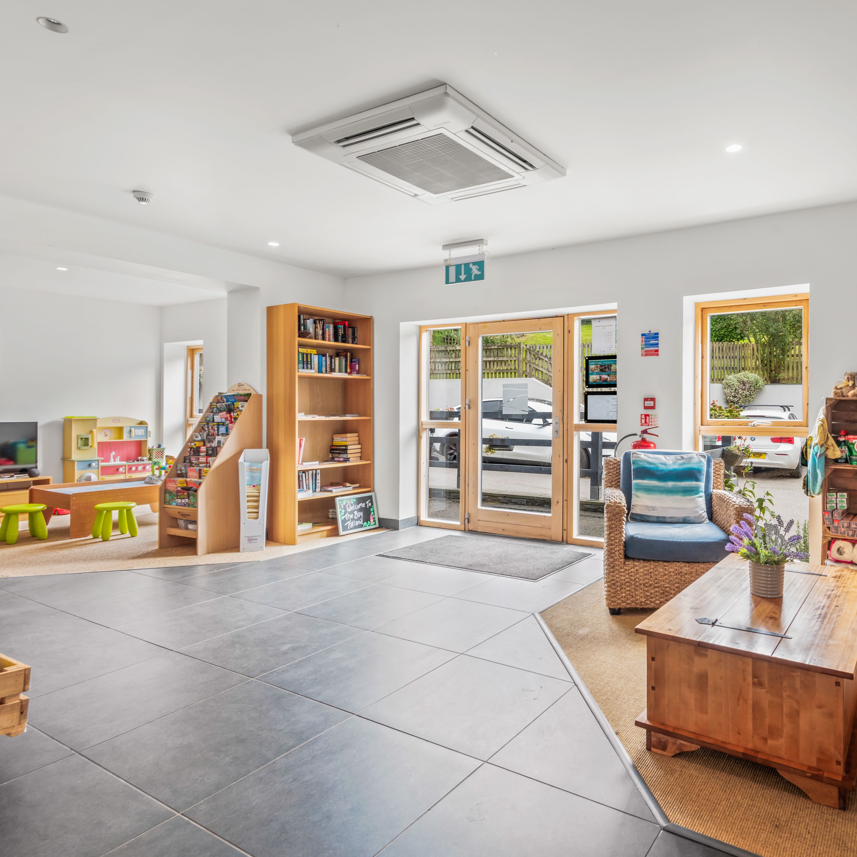 Bright and inviting family lounge area with wicker chairs, wooden shelves, children's play area, and bookcases.