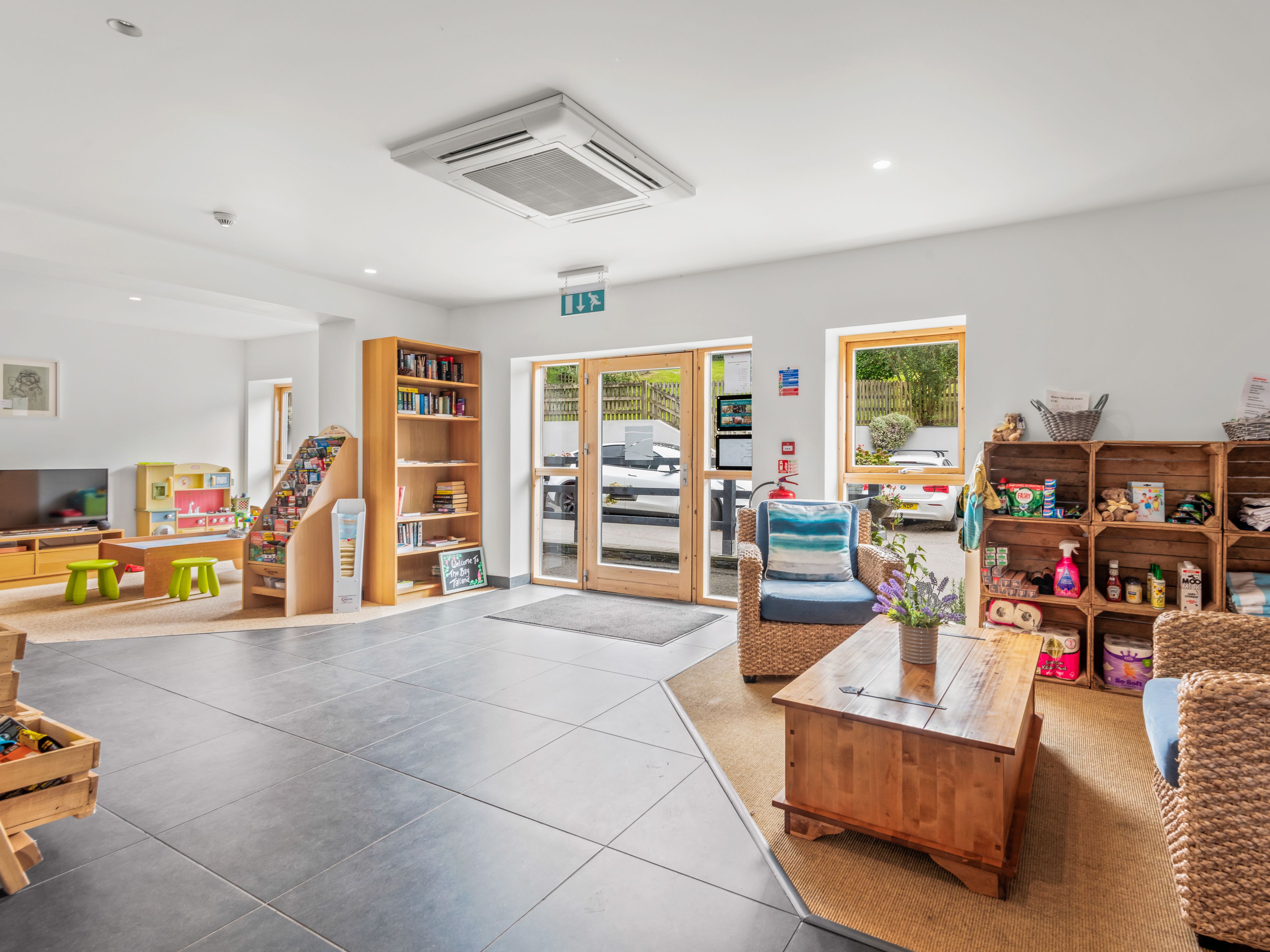 Bright and inviting family lounge area with wicker chairs, wooden shelves, children's play area, and bookcases.