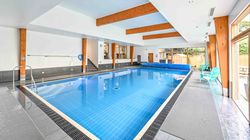 Modern indoor swimming pool with wooden beams and turquoise chairs