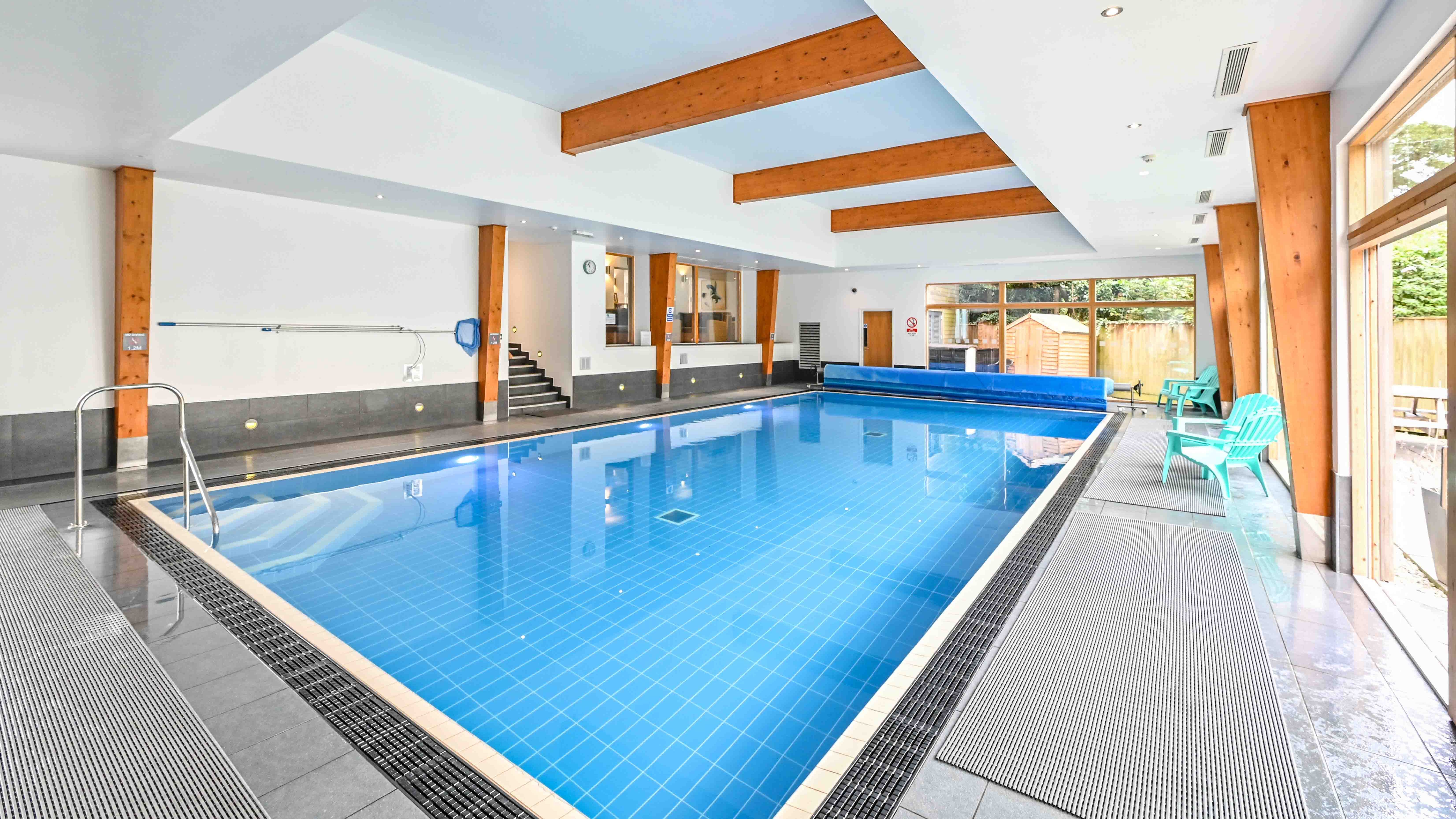 Modern indoor swimming pool with wooden beams and turquoise chairs