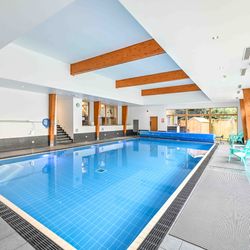 Modern indoor swimming pool with wooden beams and turquoise chairs