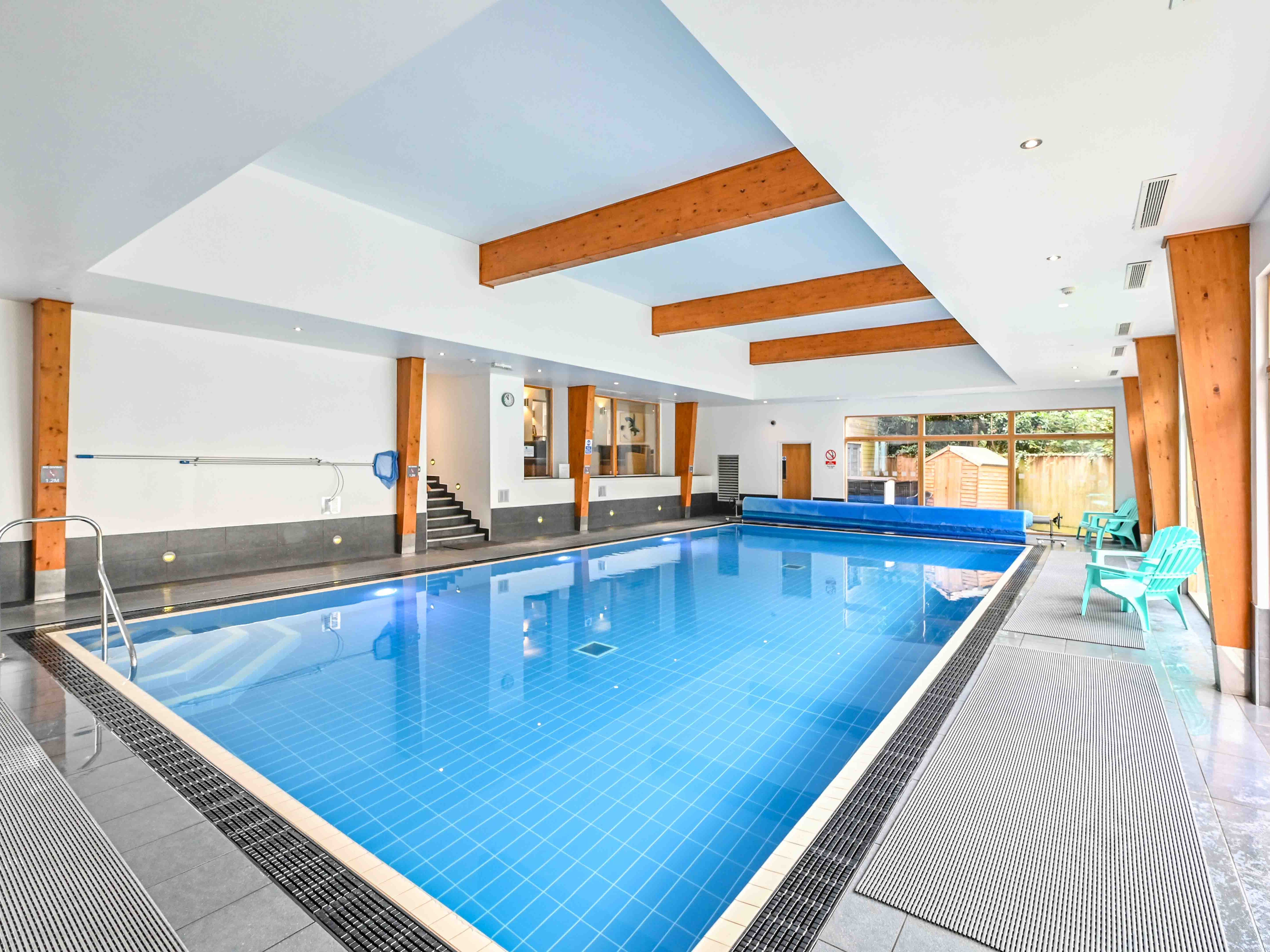 Modern indoor swimming pool with wooden beams and turquoise chairs