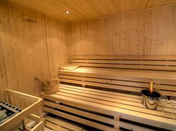 Interior of a wooden sauna with benches, a wooden bucket, and a bottle of champagne with glasses.