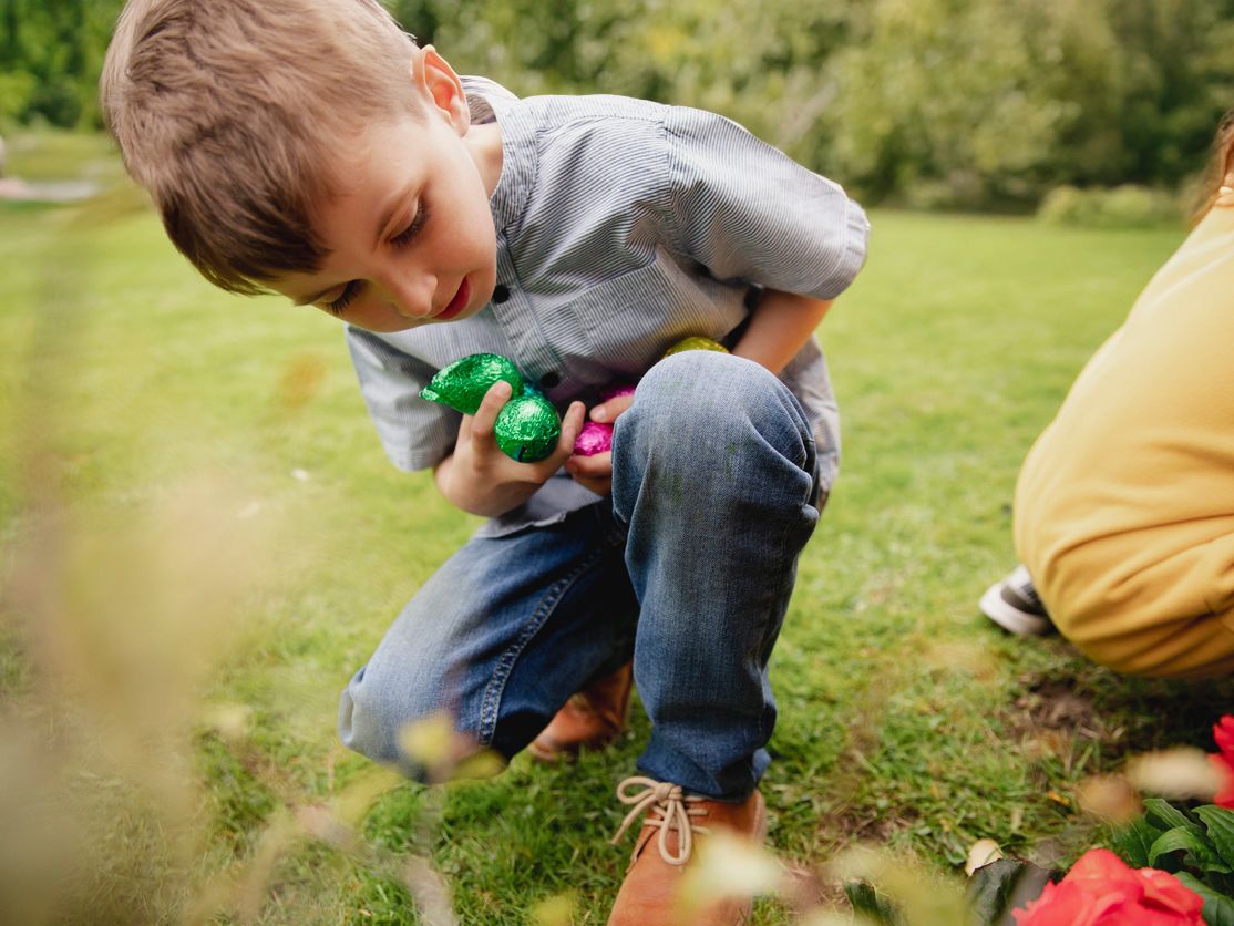 Young boy bending down on grass holding colorful Easter eggs