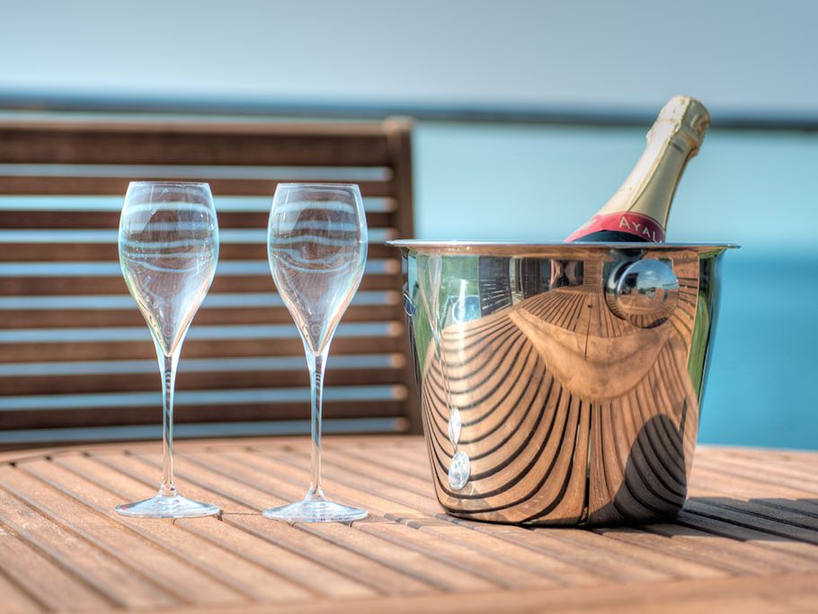 Two empty champagne glasses and a bucket with a champagne bottle on a wooden table with a blurred outdoor background.