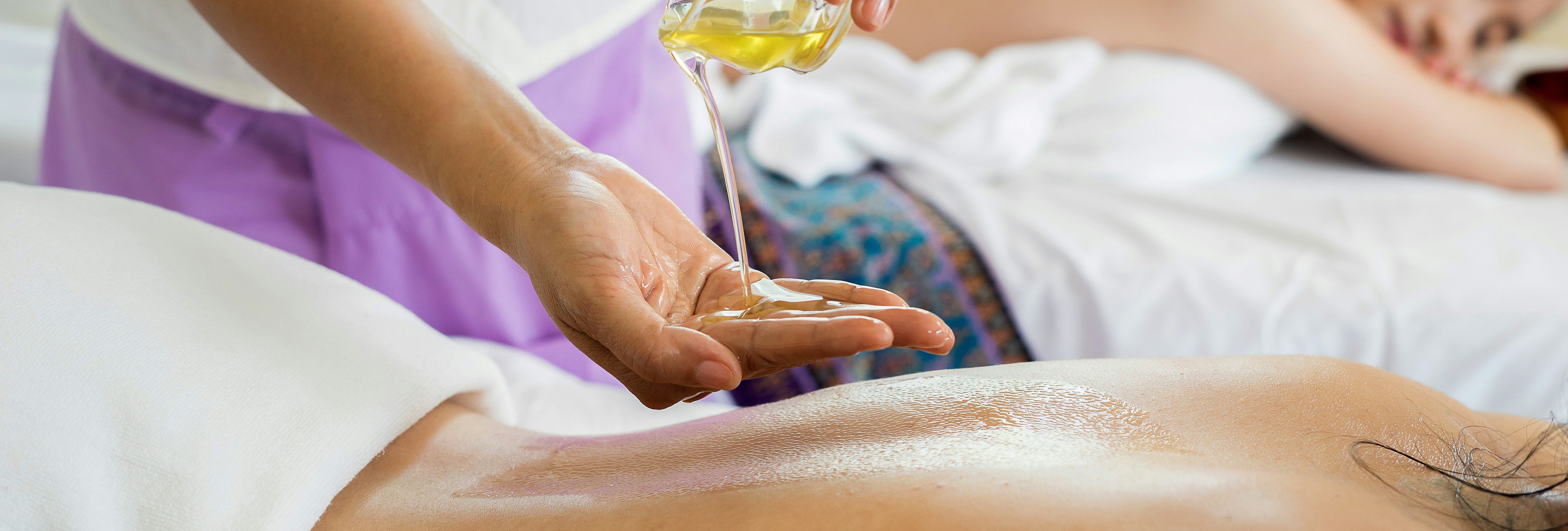 Massage therapist pouring oil on a person's back