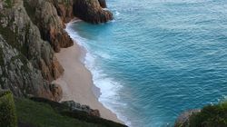A secluded sandy beach surrounded by rocky cliffs and turquoise blue ocean waves.