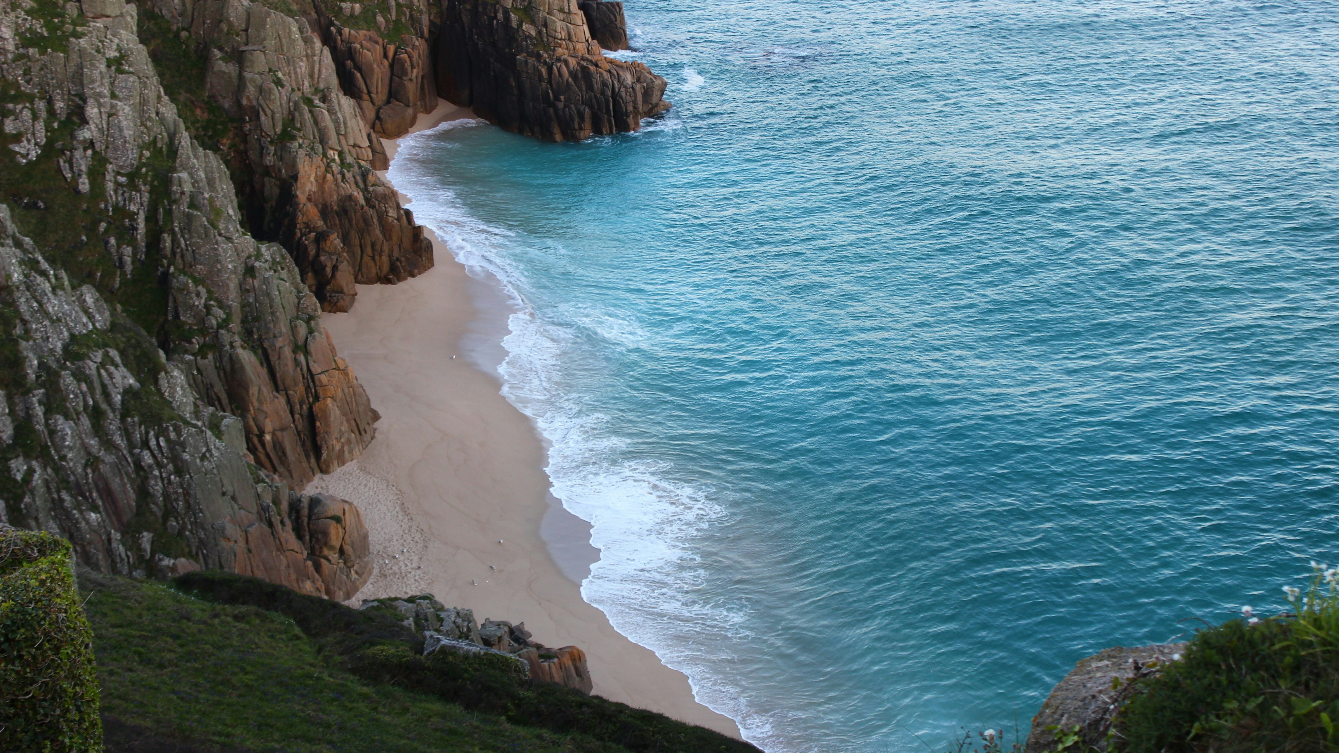 A secluded sandy beach surrounded by rocky cliffs and turquoise blue ocean waves.
