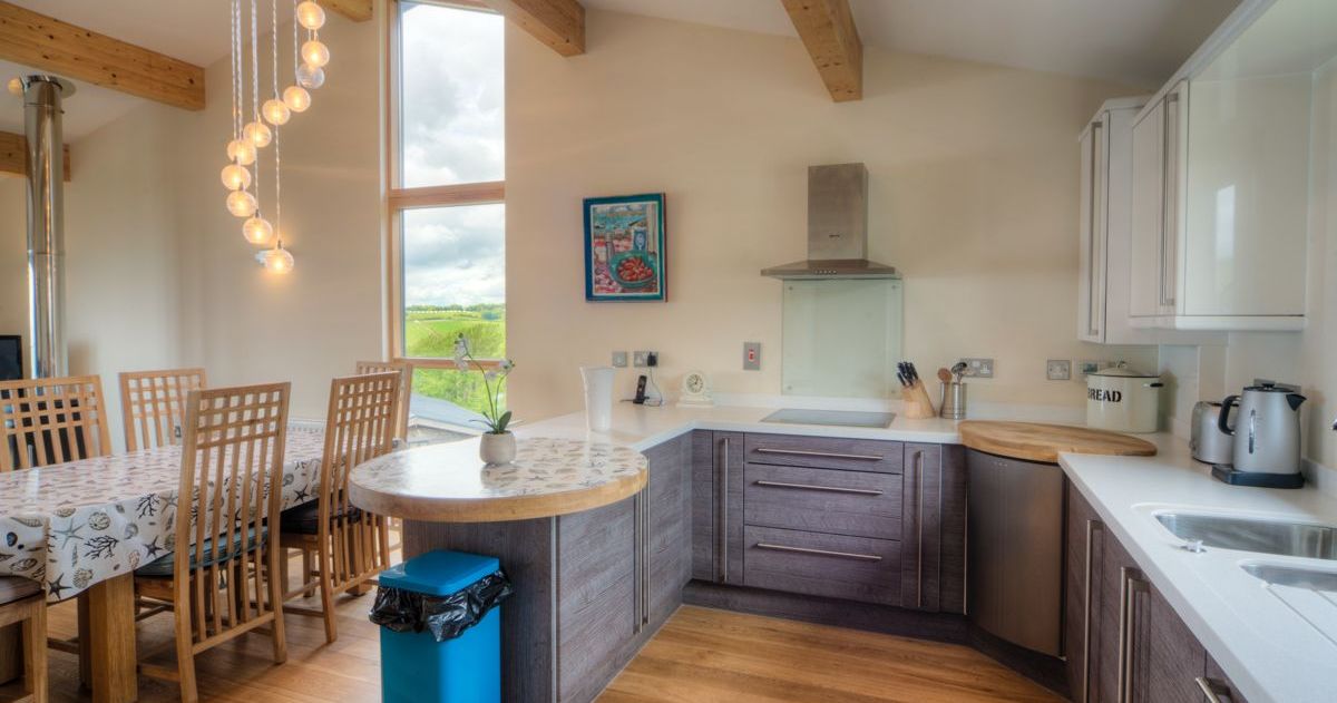 Modern kitchen and dining area with wooden beams, contemporary lighting, and large window.