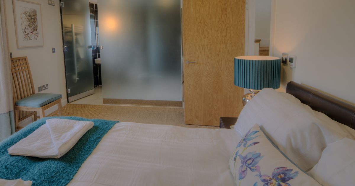 Modern bedroom with bed, teal lamp, and frosted glass bathroom wall