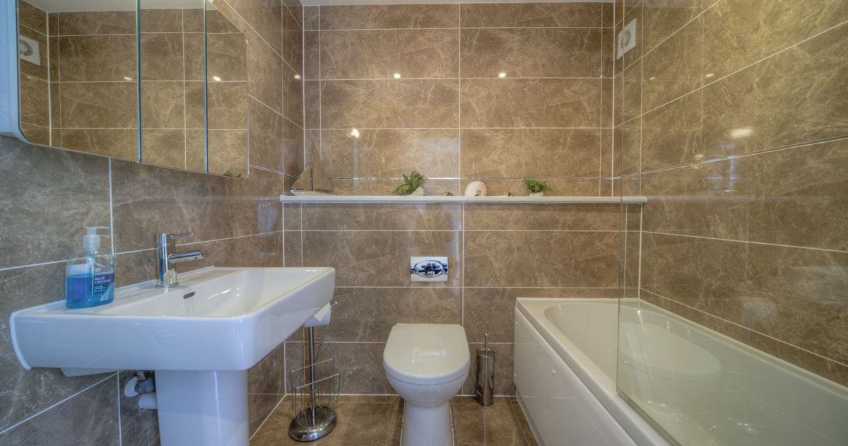 Modern bathroom with brown marble tiles, a bathtub, sink, and toilet