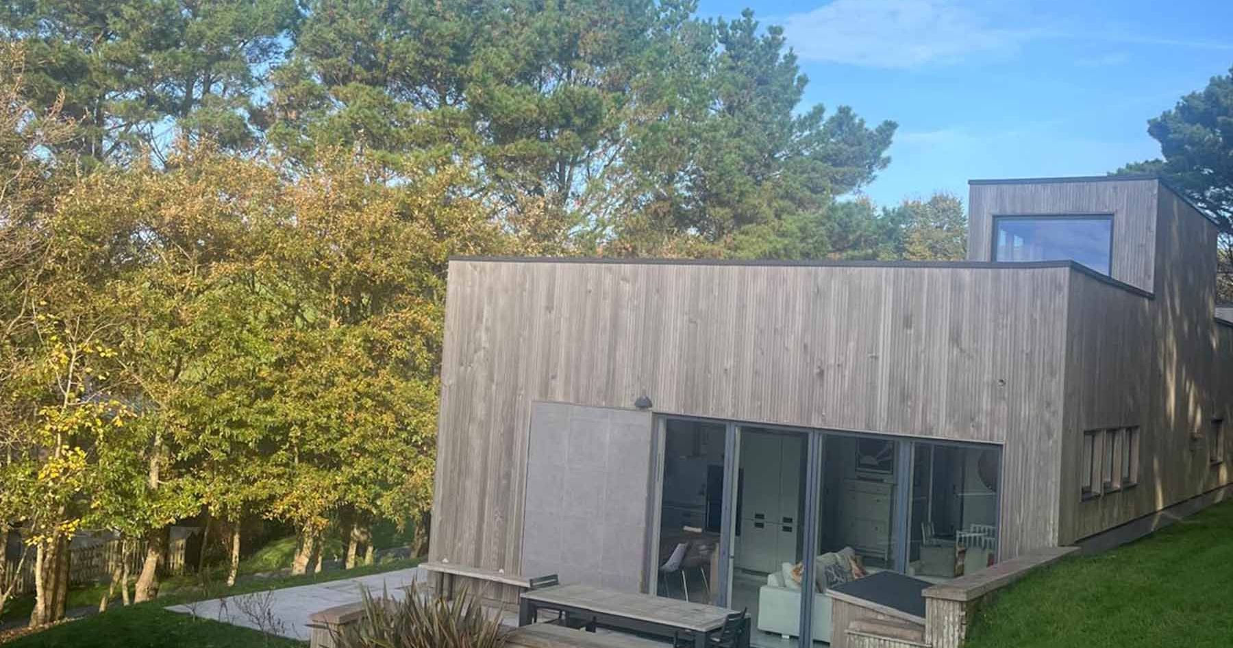 Modern wooden house with large windows surrounded by trees and grass