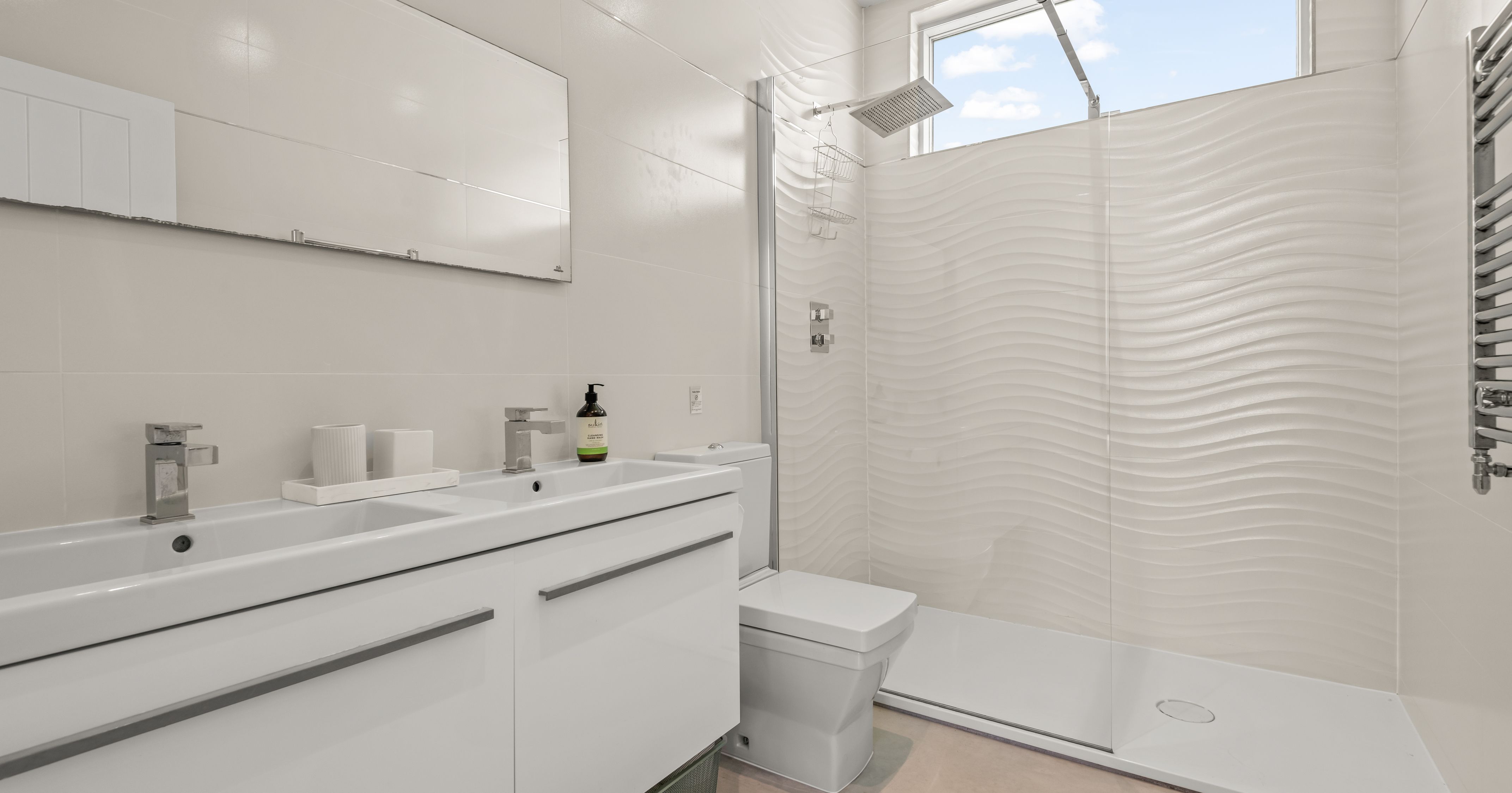 Modern white bathroom with double sink, toilet, and walk-in shower