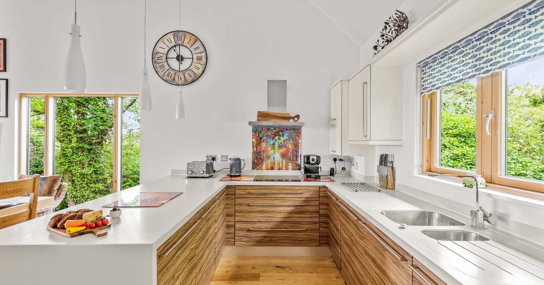 Modern kitchen with wooden cabinets, large windows, and a colorful painting behind the stove.