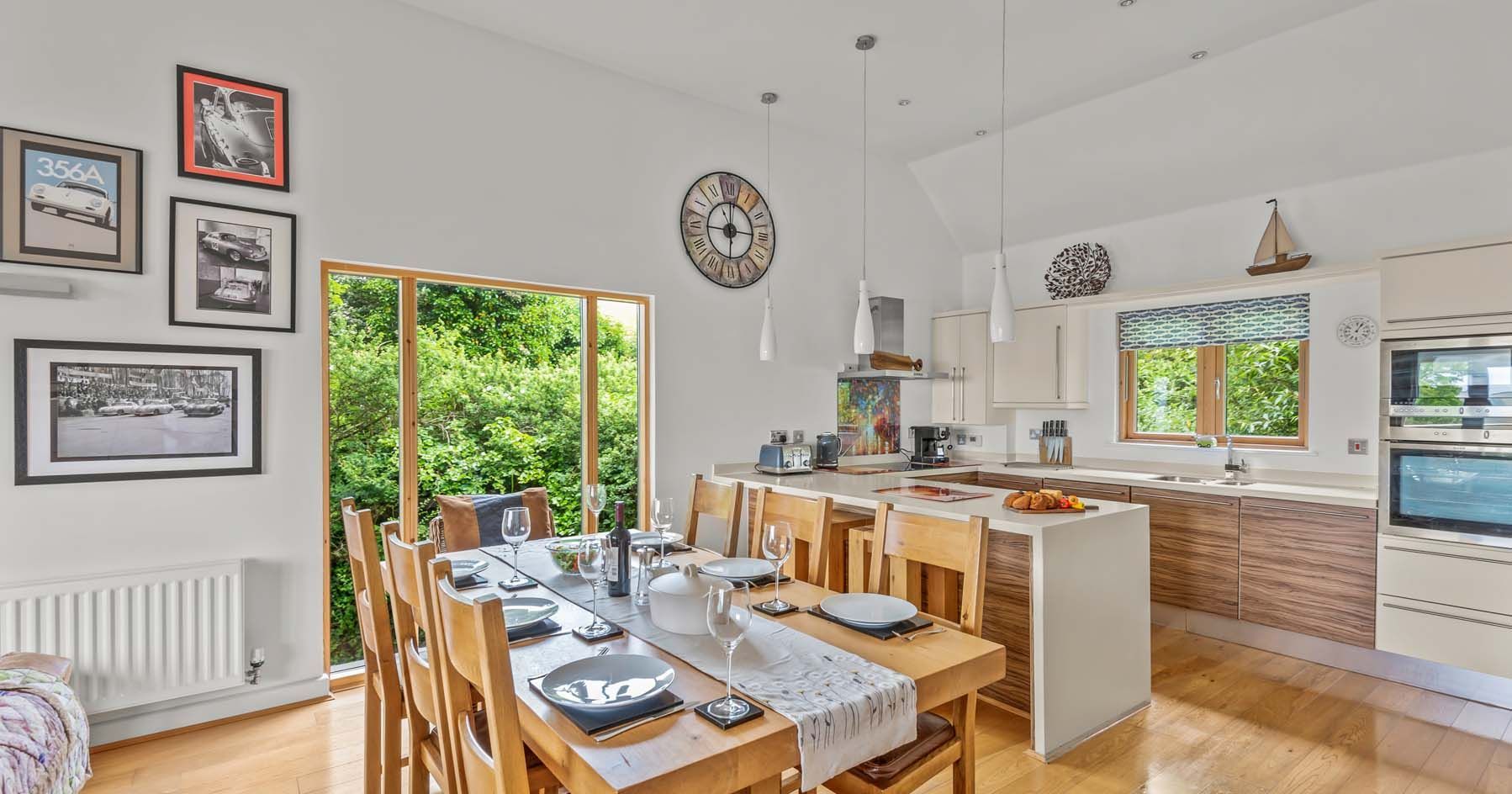 Modern kitchen and dining area with wooden table, set for six, and large windows overlooking greenery.
